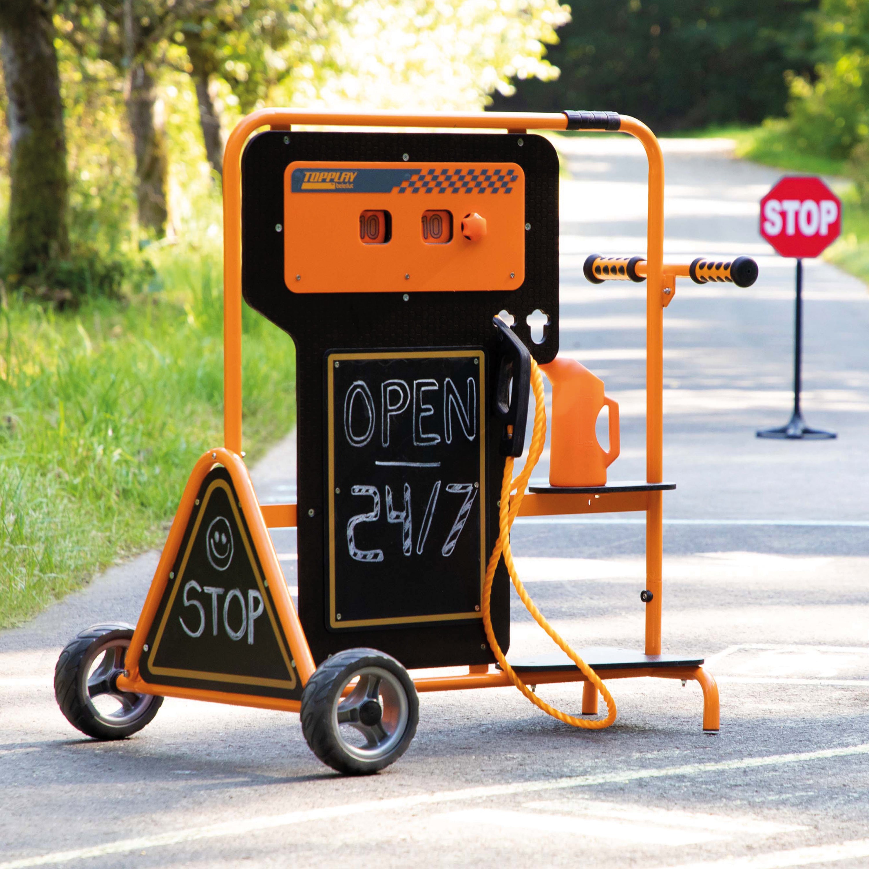 An orange and black portable fuel dump cart with a triangular stop sign on the front, set on a paved road outdoors. The cart has a chalkboard sign reading 'OPEN 24/7' and an orange fuel container attached to the side.
