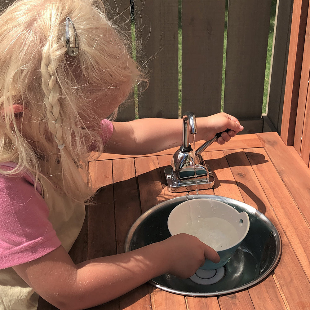Child washing a blue cup in an outdoor sink.