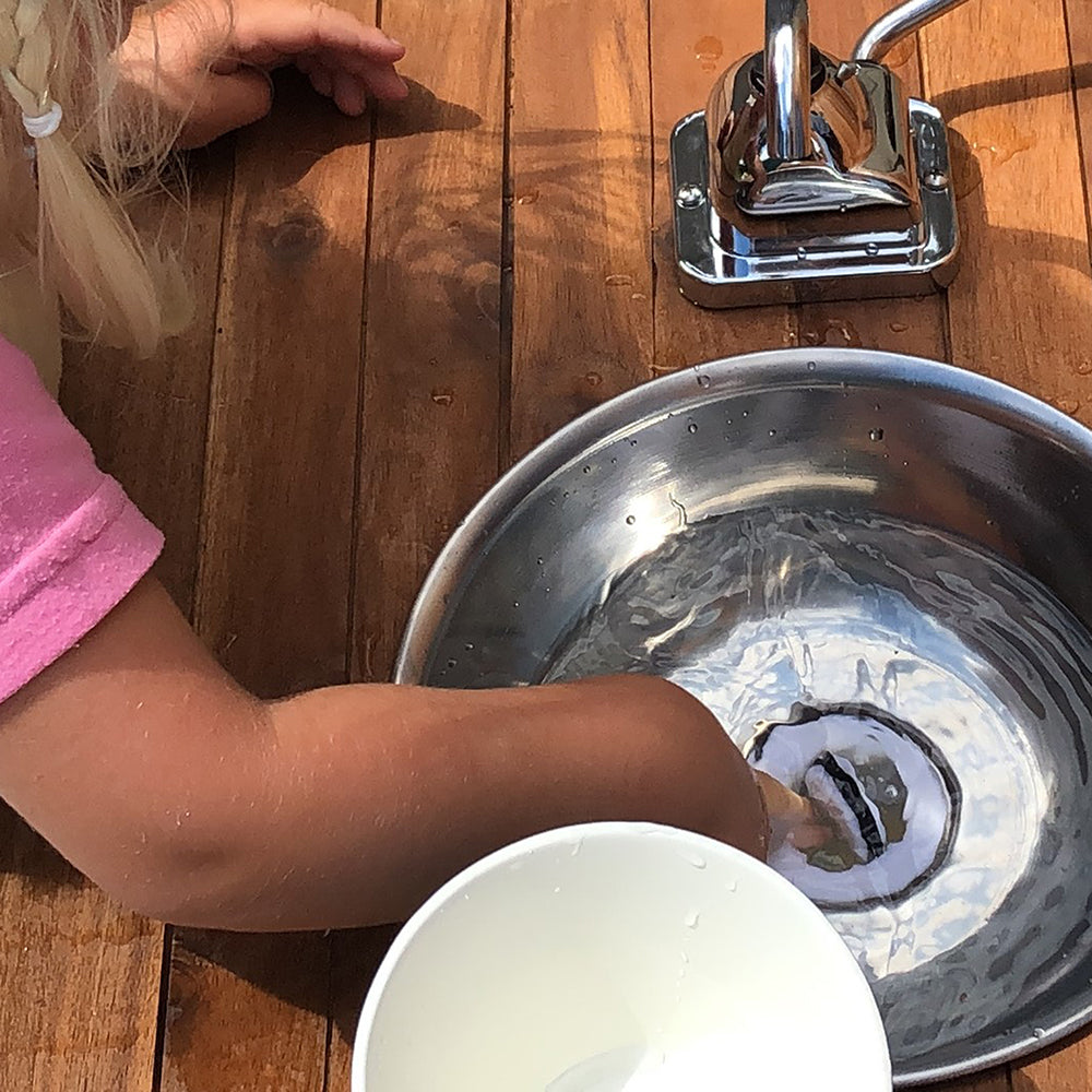Person washing a dish in a metal sink with a wooden background