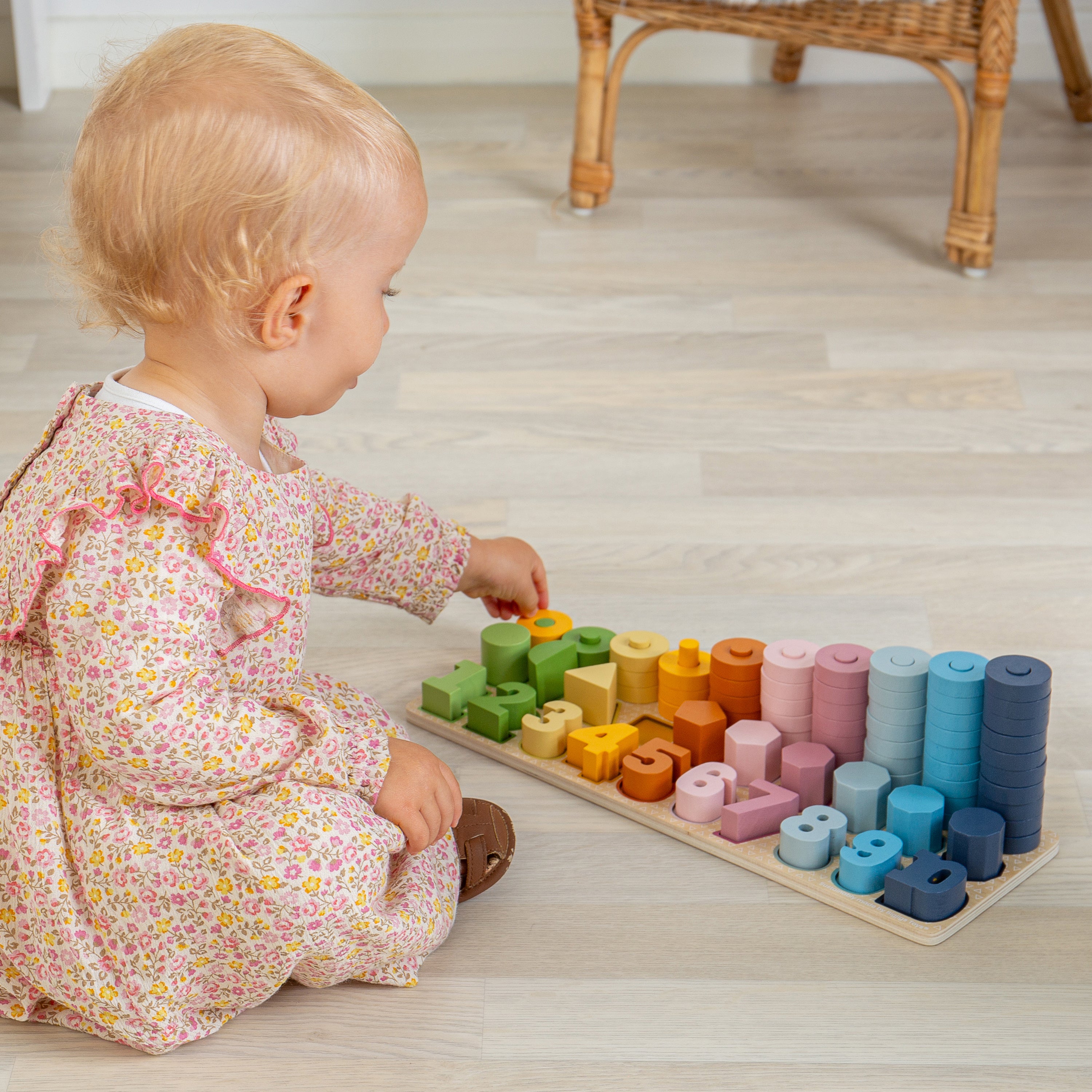 Child playing with a colorful wooden sorting toy on a light wooden floor.