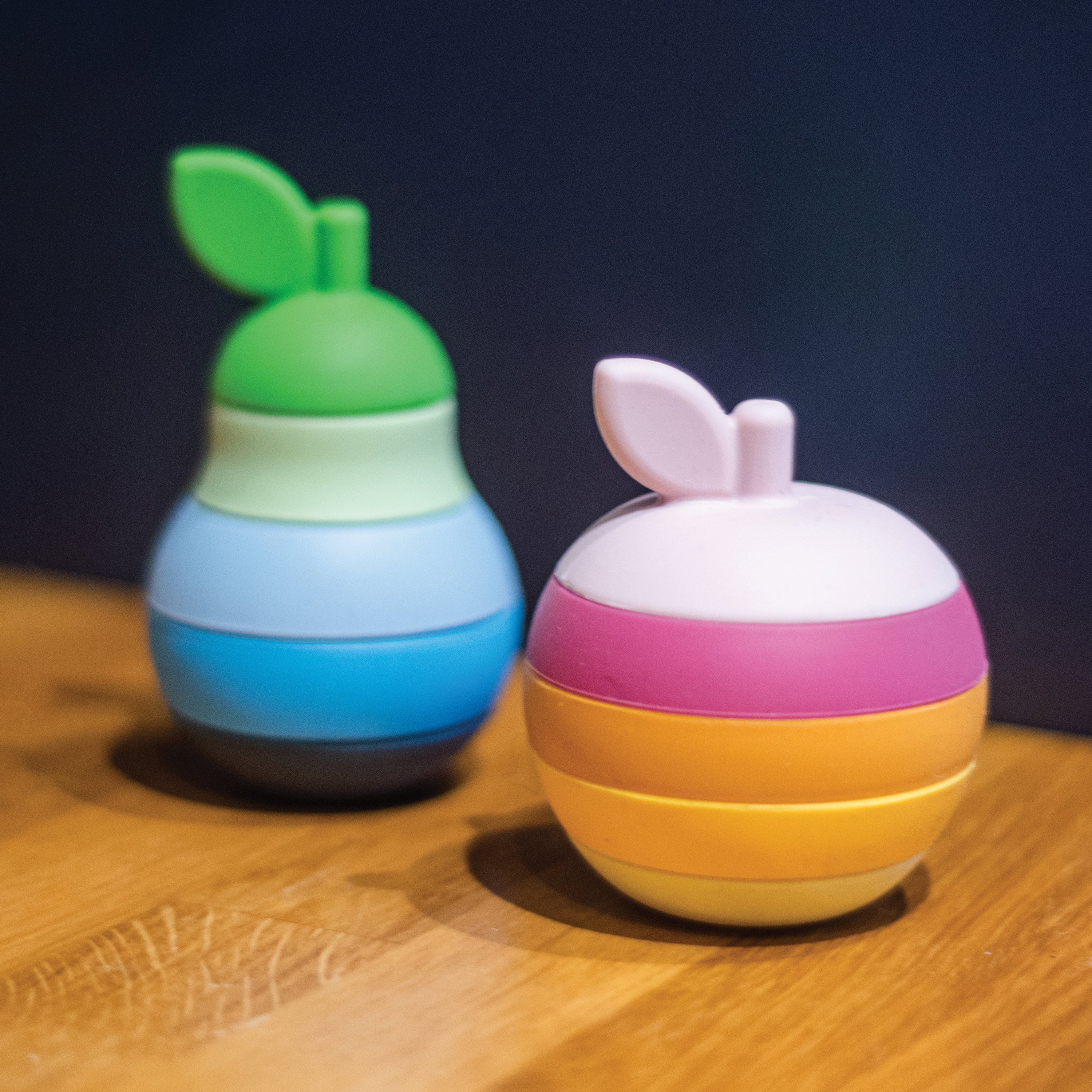 Two colorful, stacked toy figures on a wooden surface with a dark background