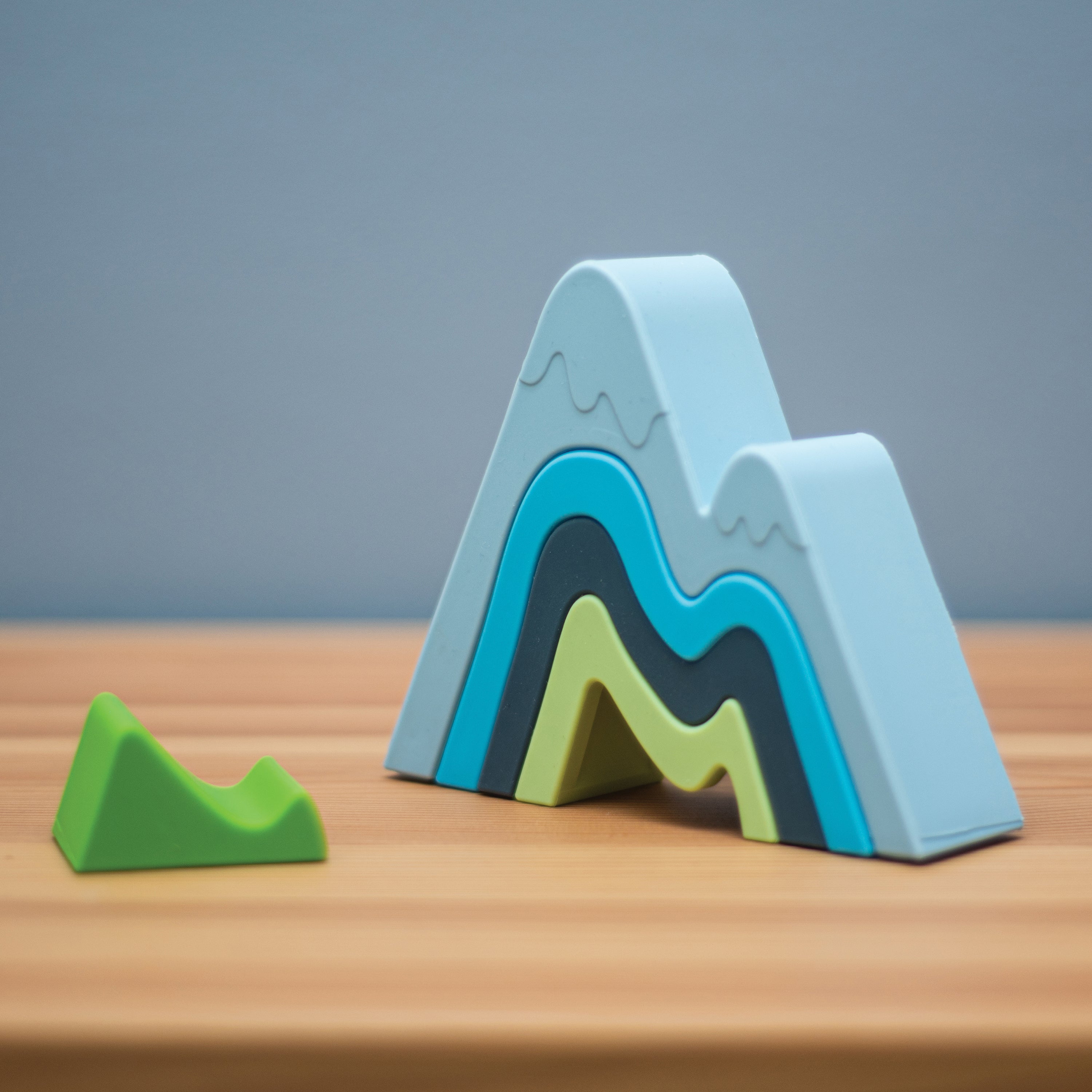 Colorful mountain-shaped foam blocks on a wooden surface with a gray background