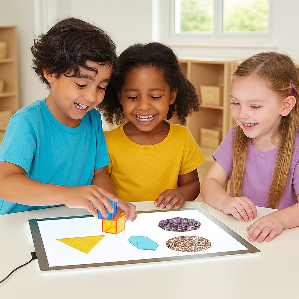 Three children playing with geometric shapes on a lightboard in a classroom setting.
