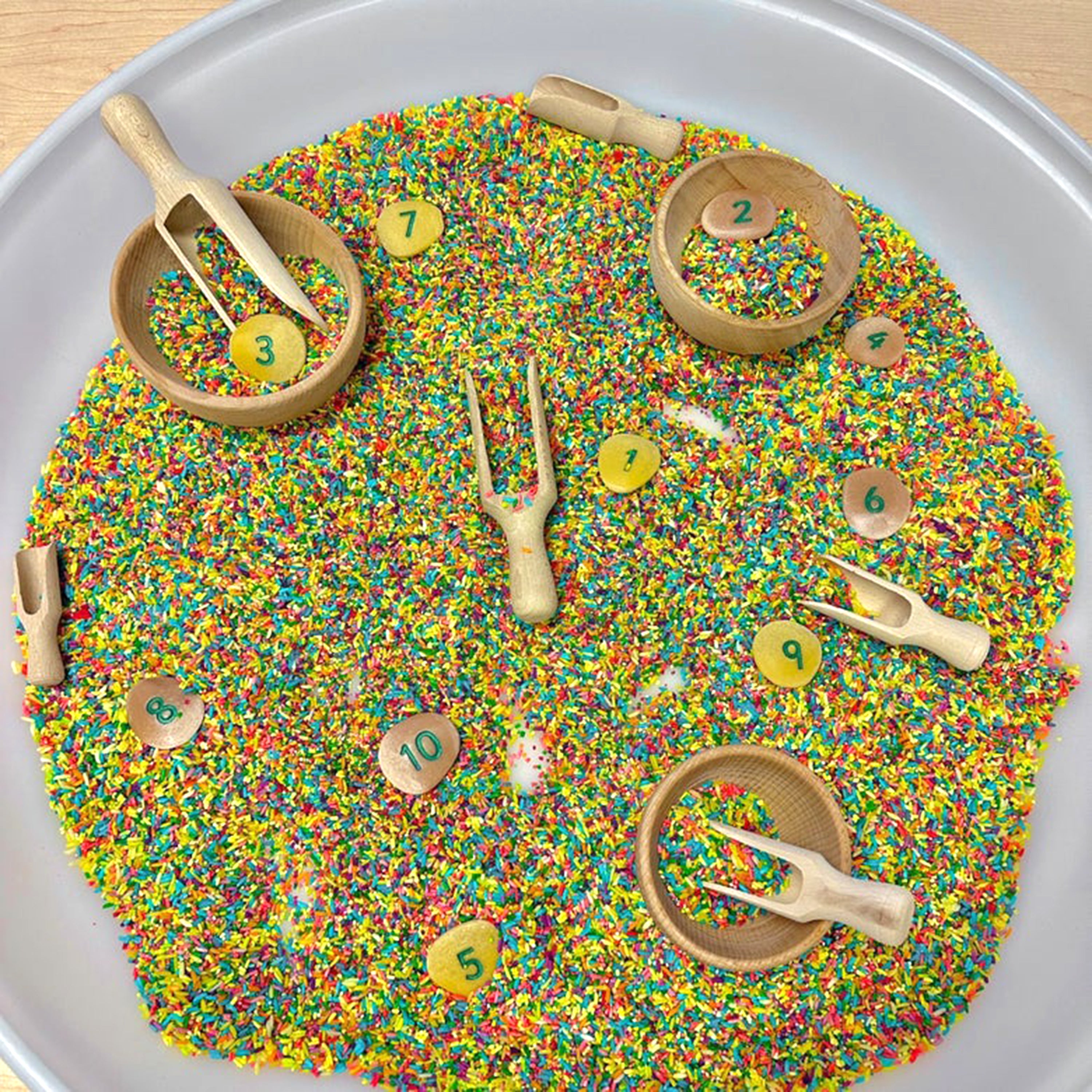 Colorful sprinkles with wooden toys and numbered buttons on a white tray