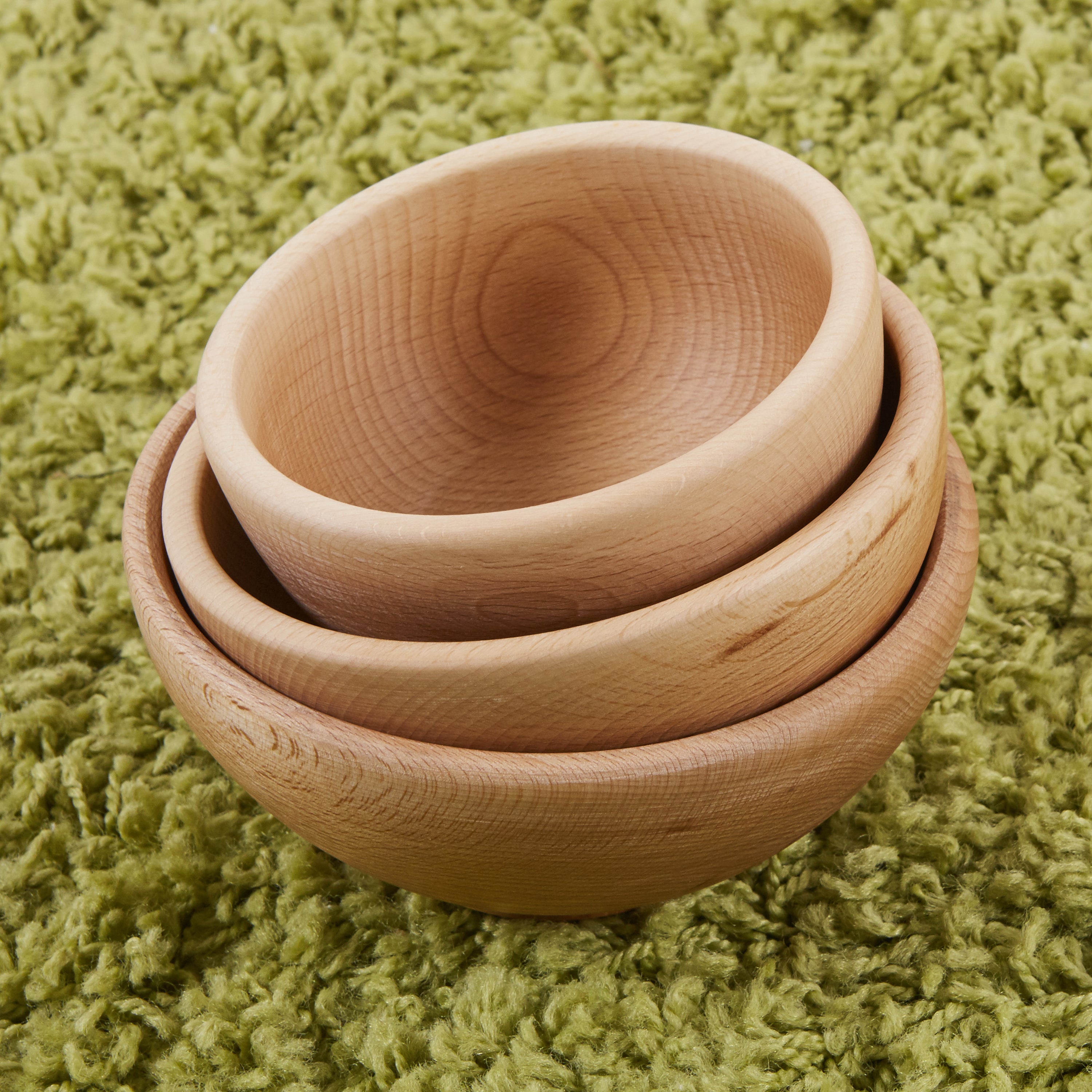 Three wooden bowls stacked on a green textured surface