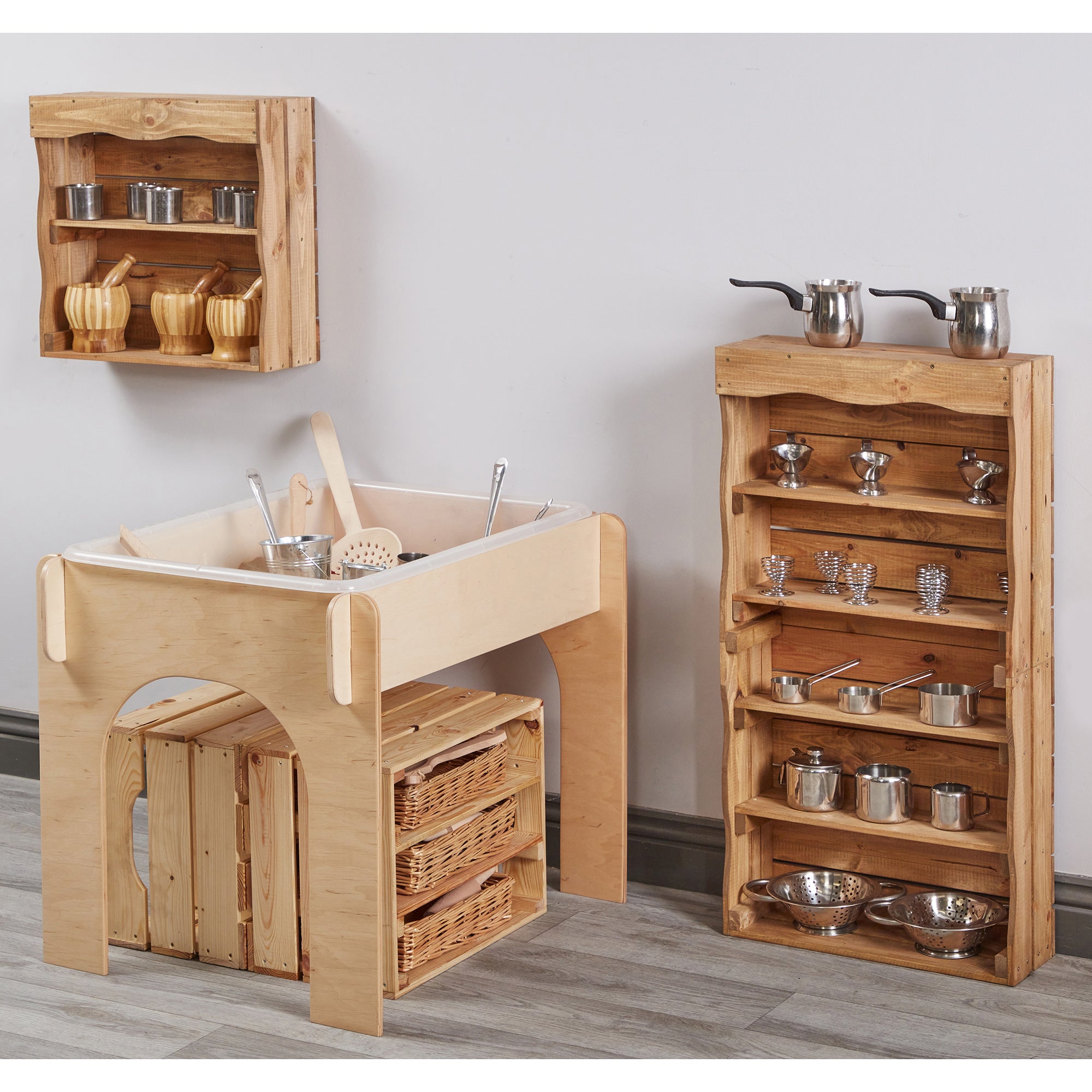 Wooden play kitchen set with shelves and utensils on a gray floor.