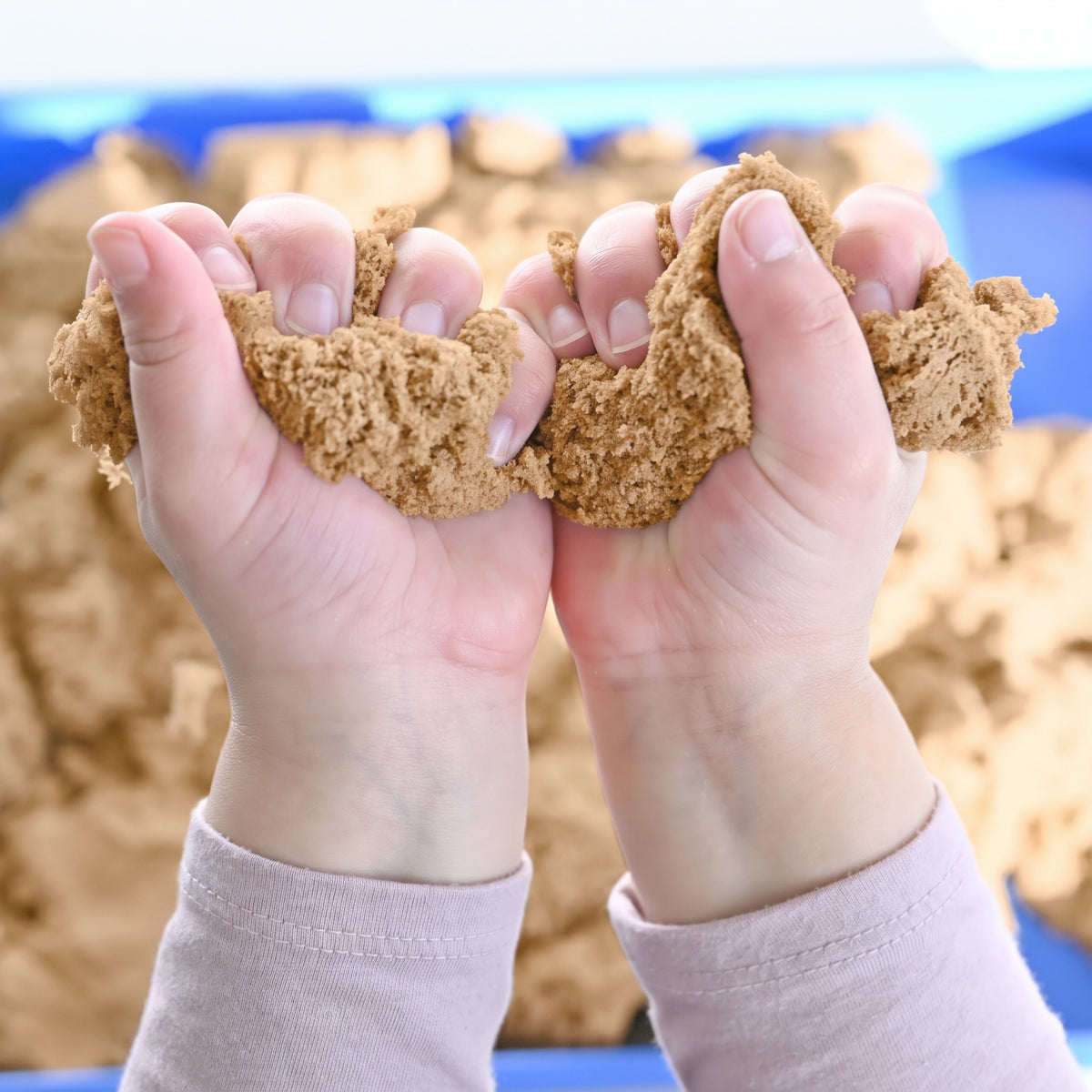 Child squeezing Wonder Flow Sensory Sand with both hands during tactile sensory play