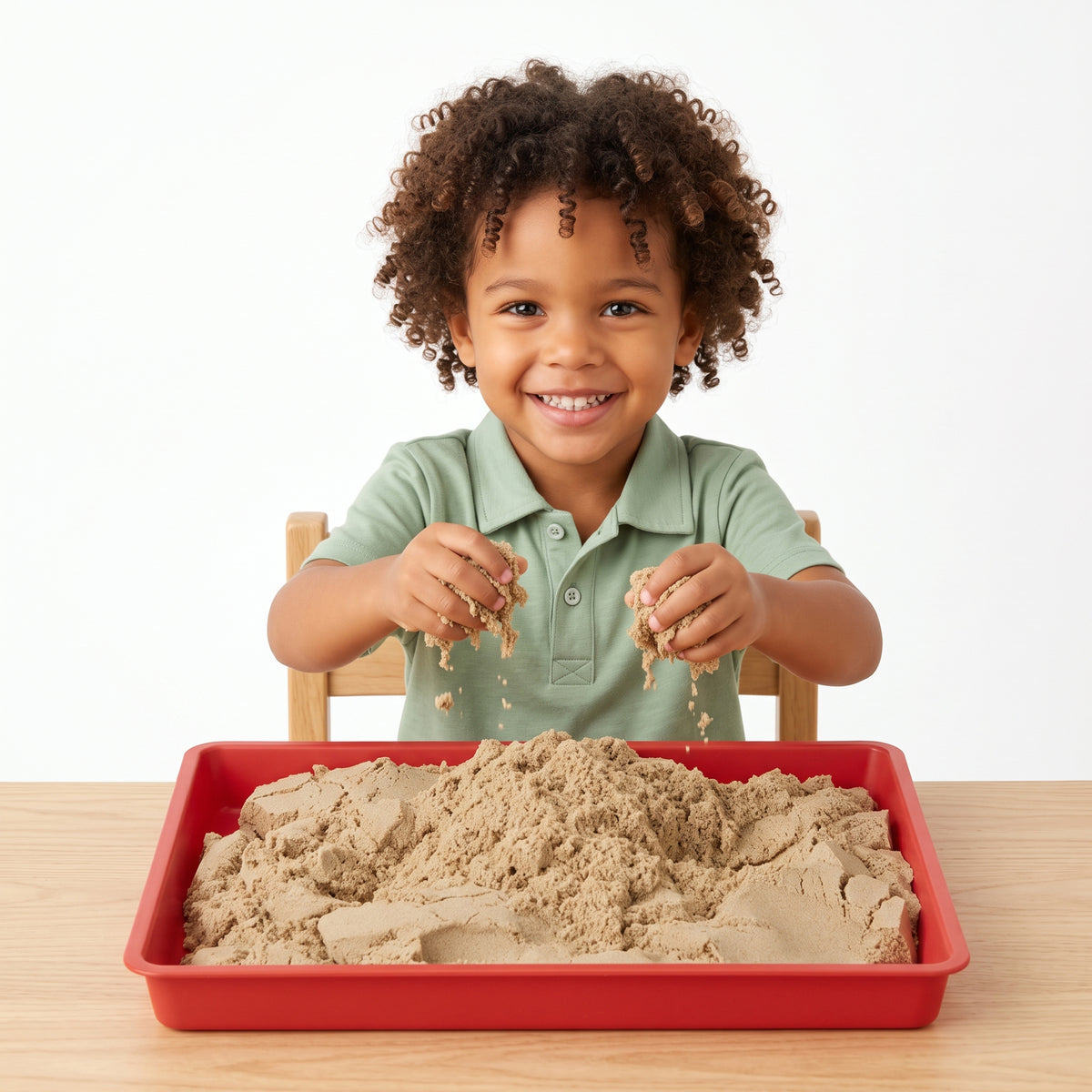 Smiling child holding moldable Wonder Flow Sensory Sand over a red sensory activity tray