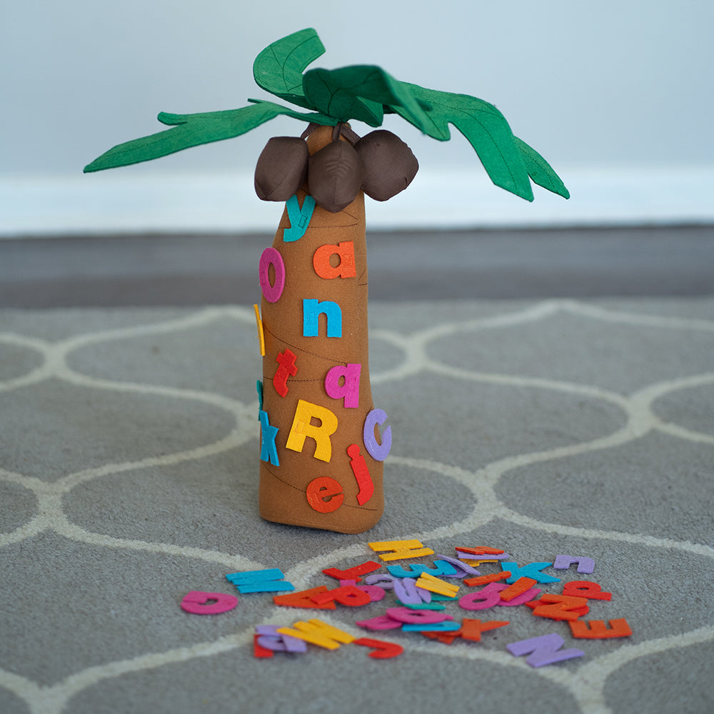 A fabric tree playset with letters adhered to it, set on a classroom carpet, part of the Chicka Chicka Boom Boom series.