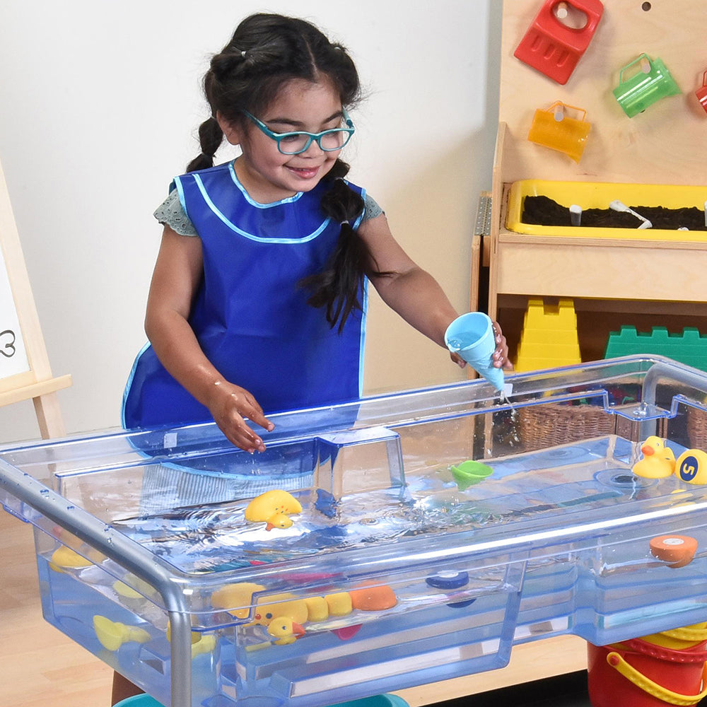 Child playing with a water table filled with toys in a classroom setting.