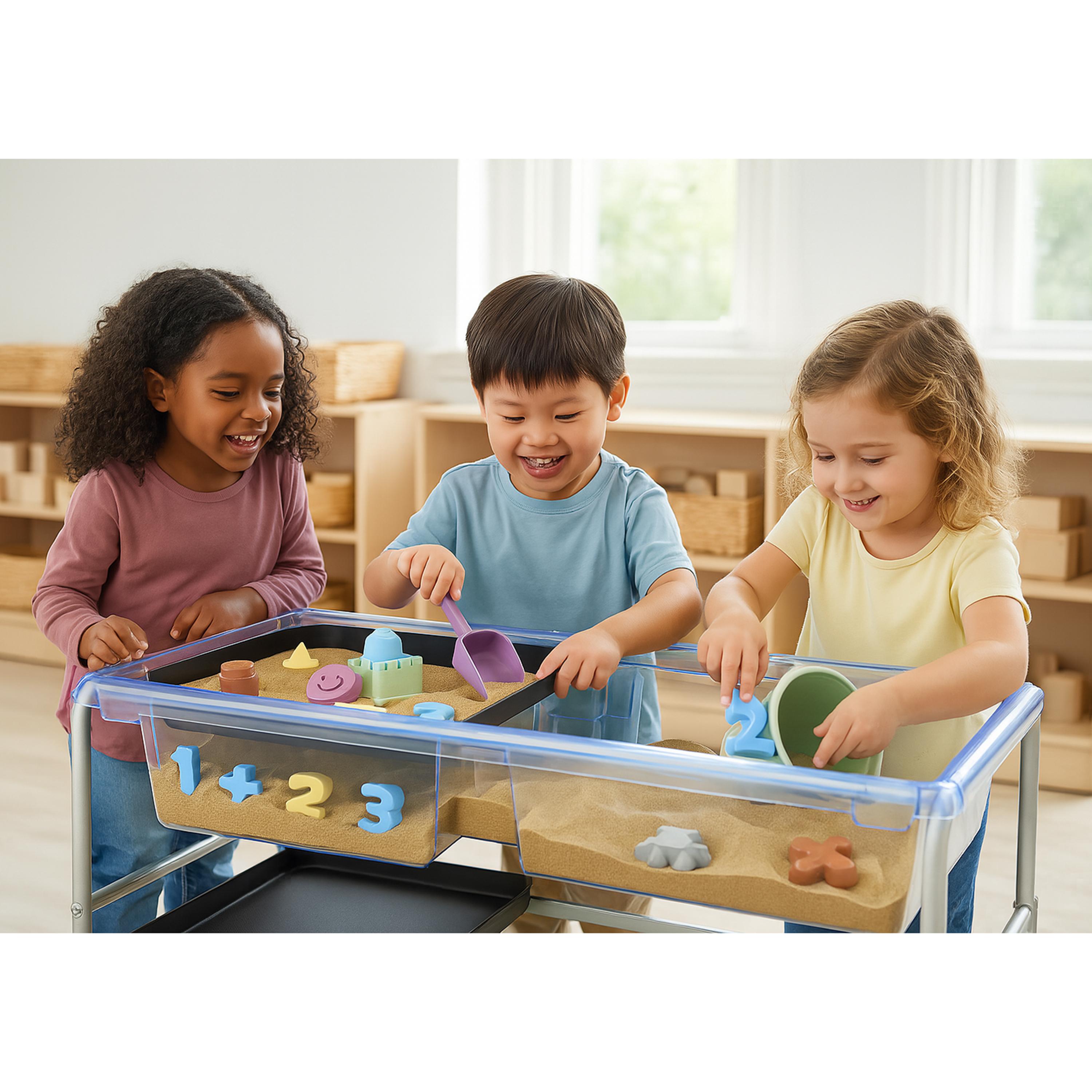 Three children playing with a transparent sandbox table in a classroom setting.