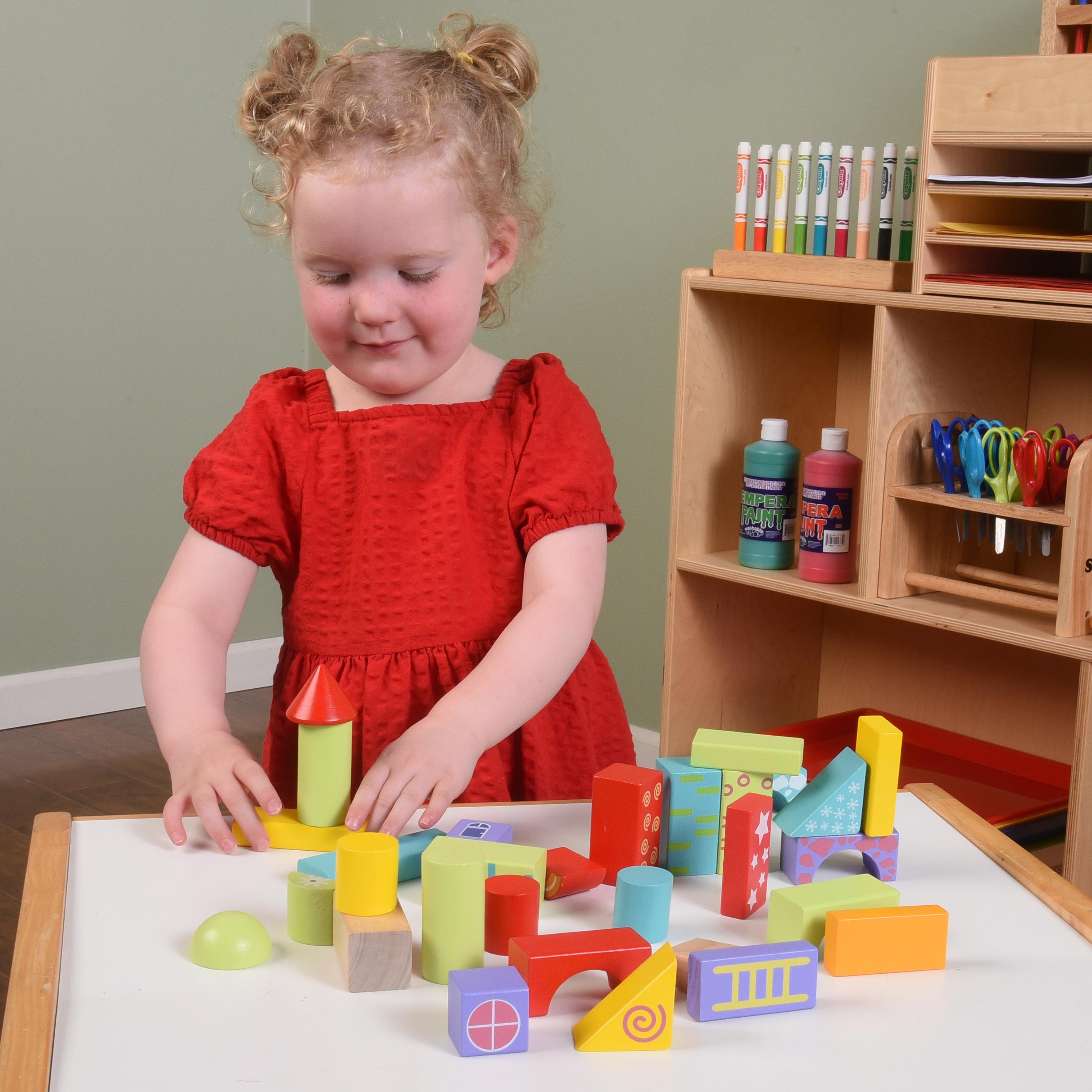 Child playing with colorful blocks at a table in a classroom setting.