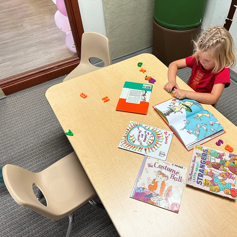 Child sitting at a table with books and colorful objects in a room.