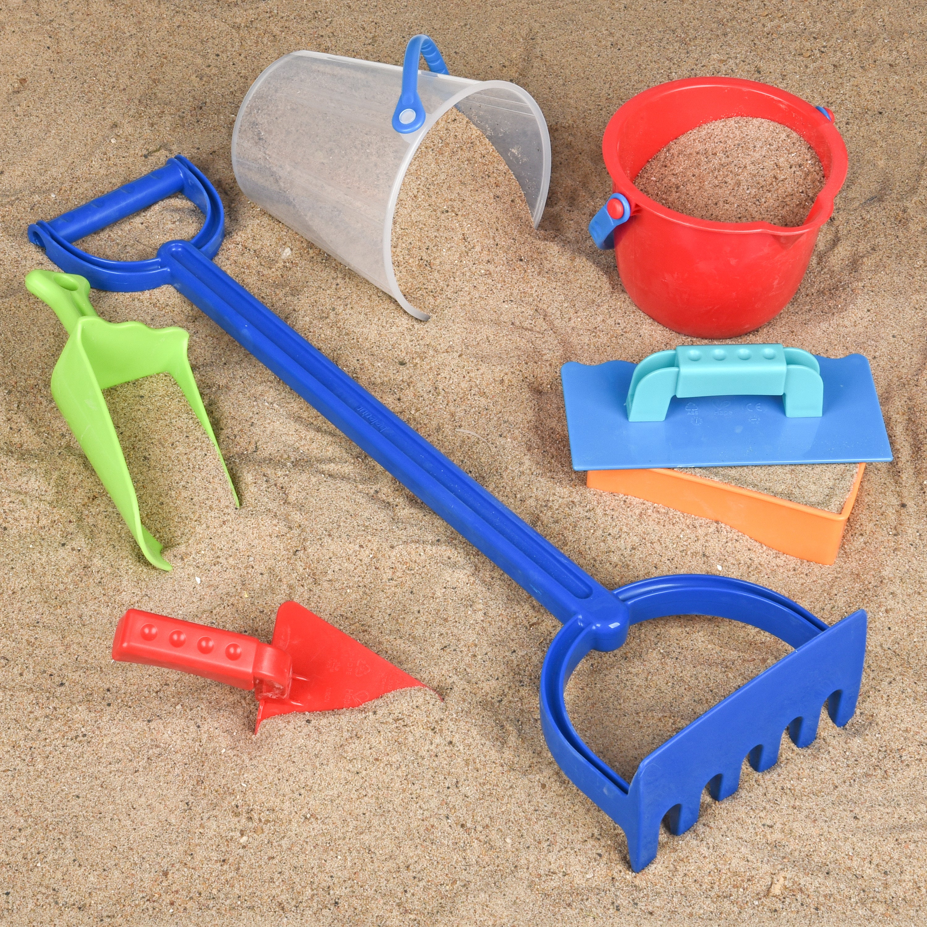 Set of colorful sand toys including a blue spade, red bucket, and various shovels on sand.