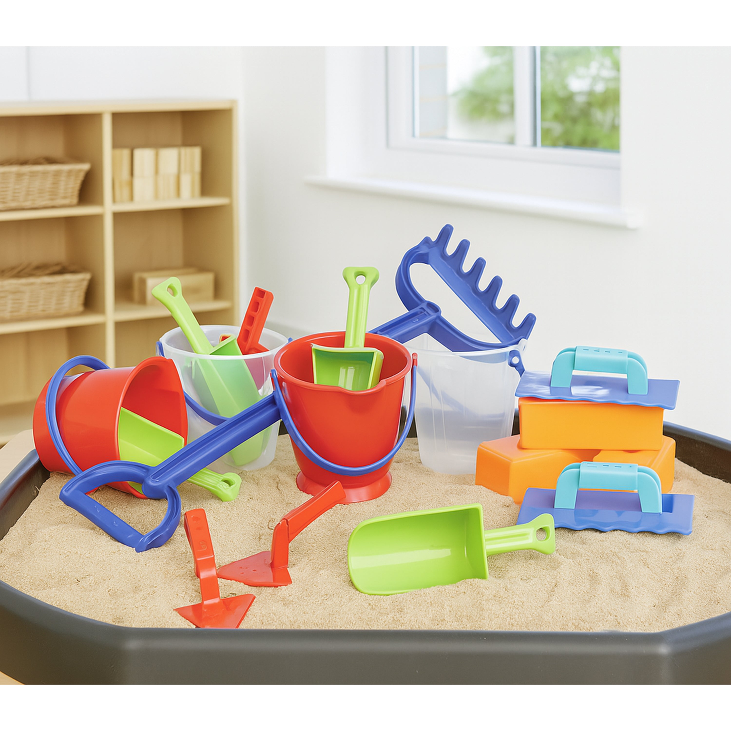 Colorful sand toys including buckets, shovels, and rakes on a sand tray indoors.