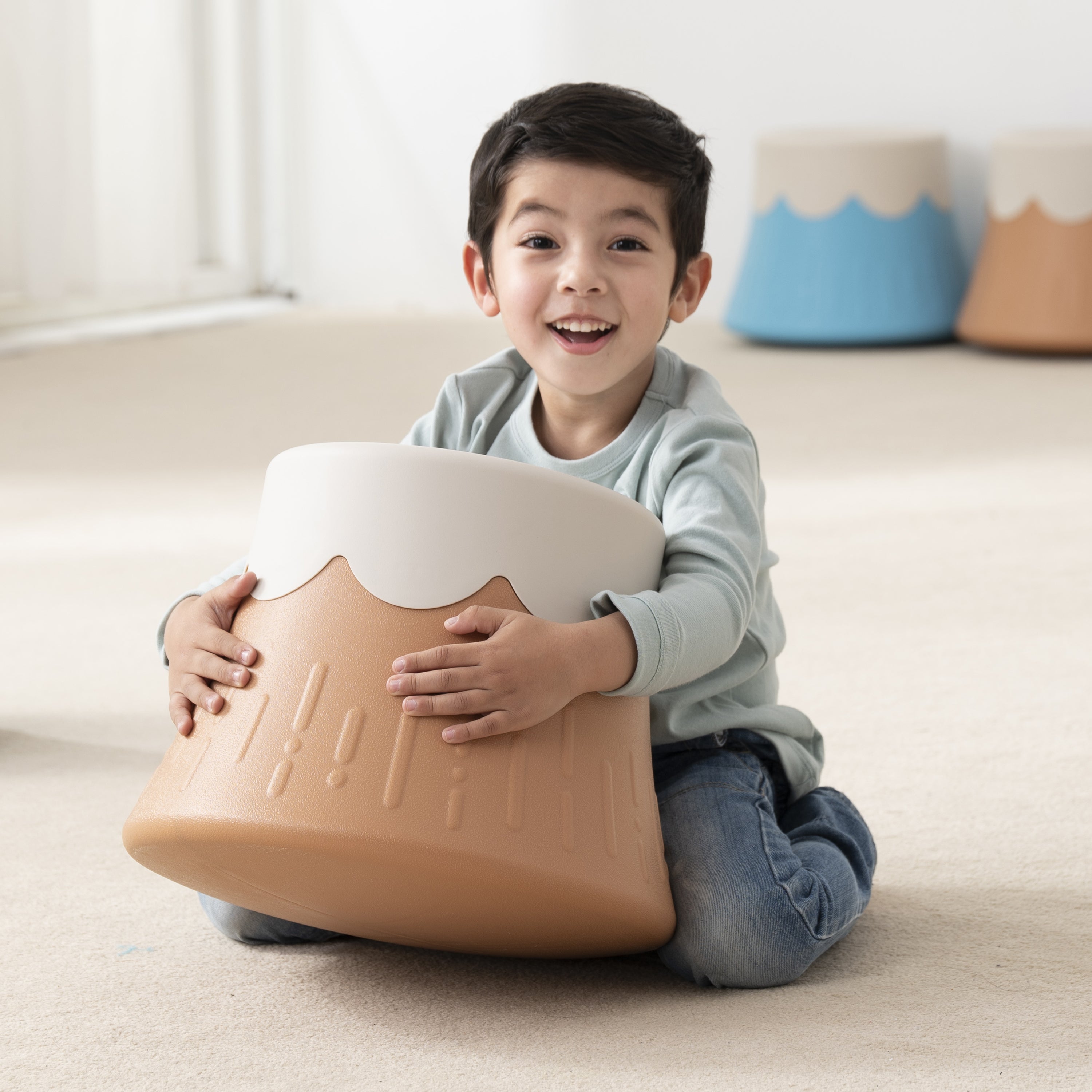 Child holding a volcano chair with a white top on a light-colored floor.