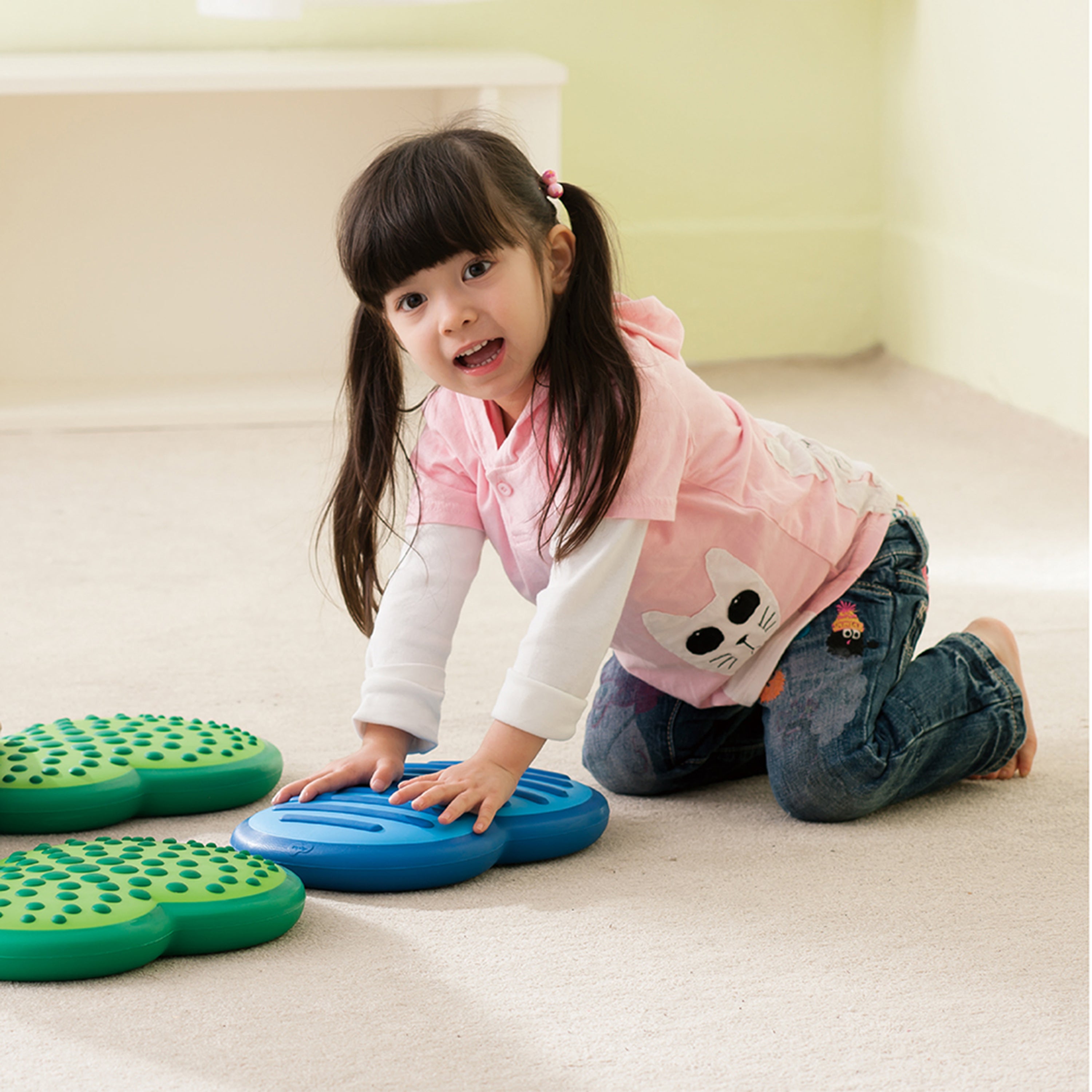 Child playing with green and blue stepping stones on a light-colored floor.