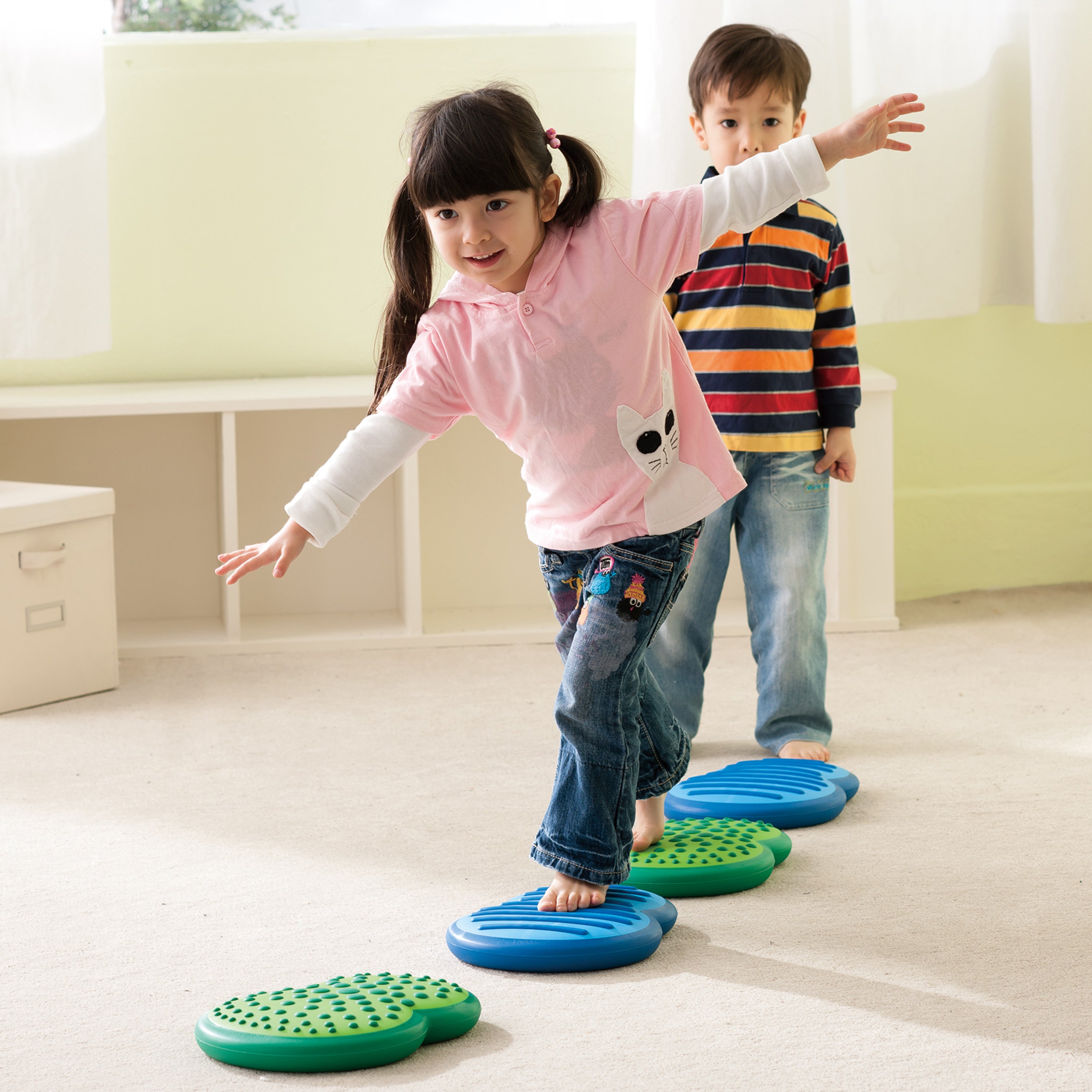 Two children playing with balance boards on a light-colored floor.