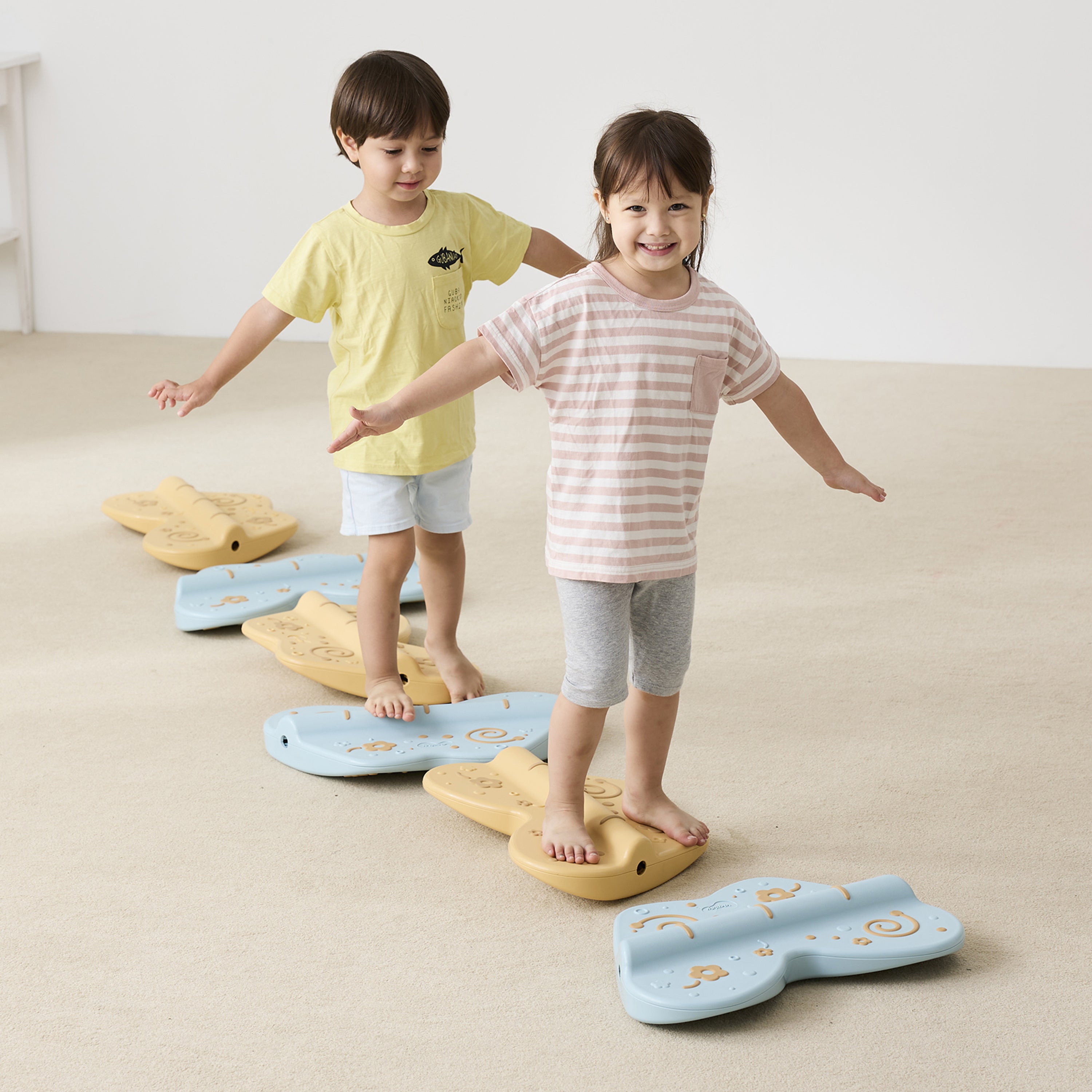 Two children standing on colorful balance boards on a beige floor.