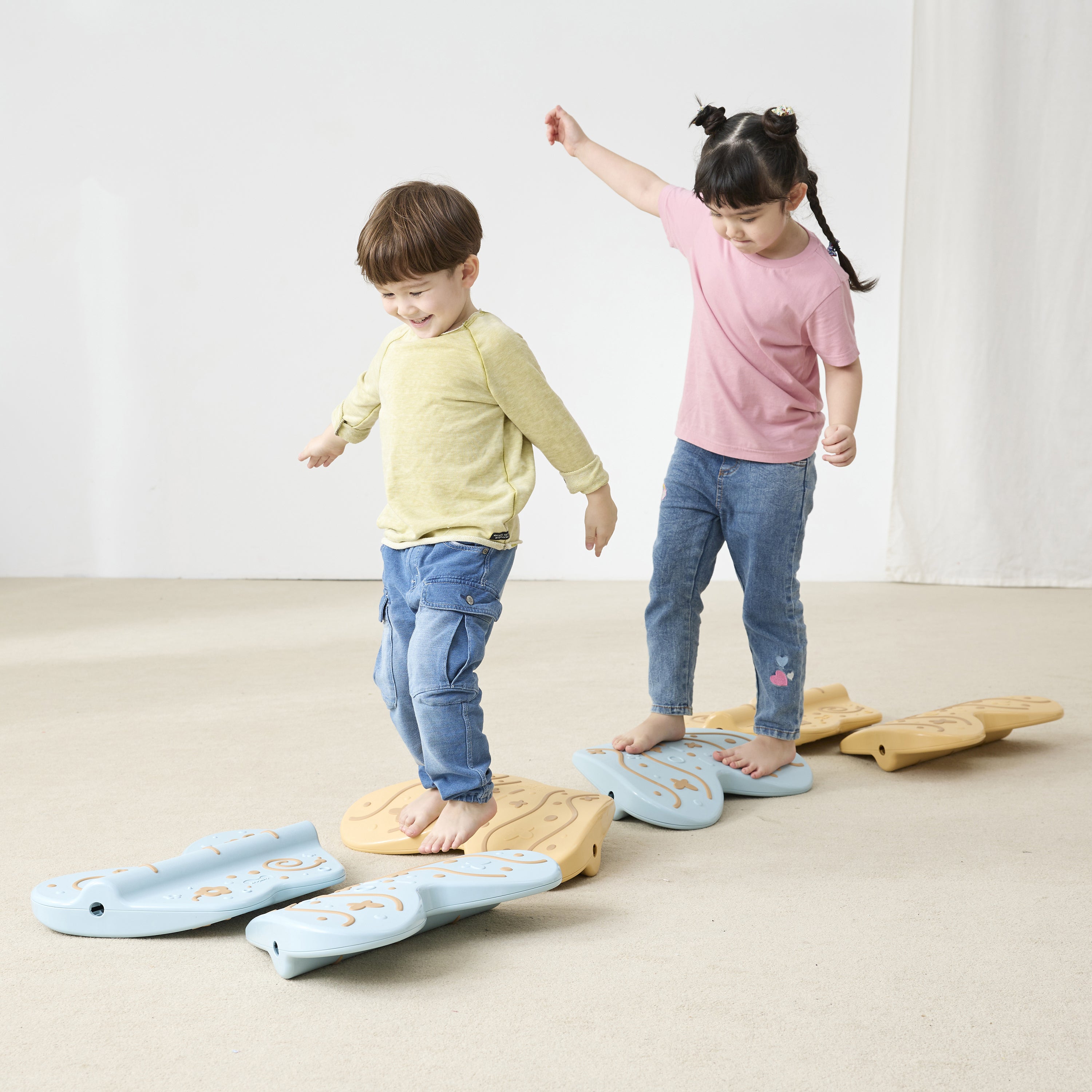 Two children standing on balance toys on a plain background