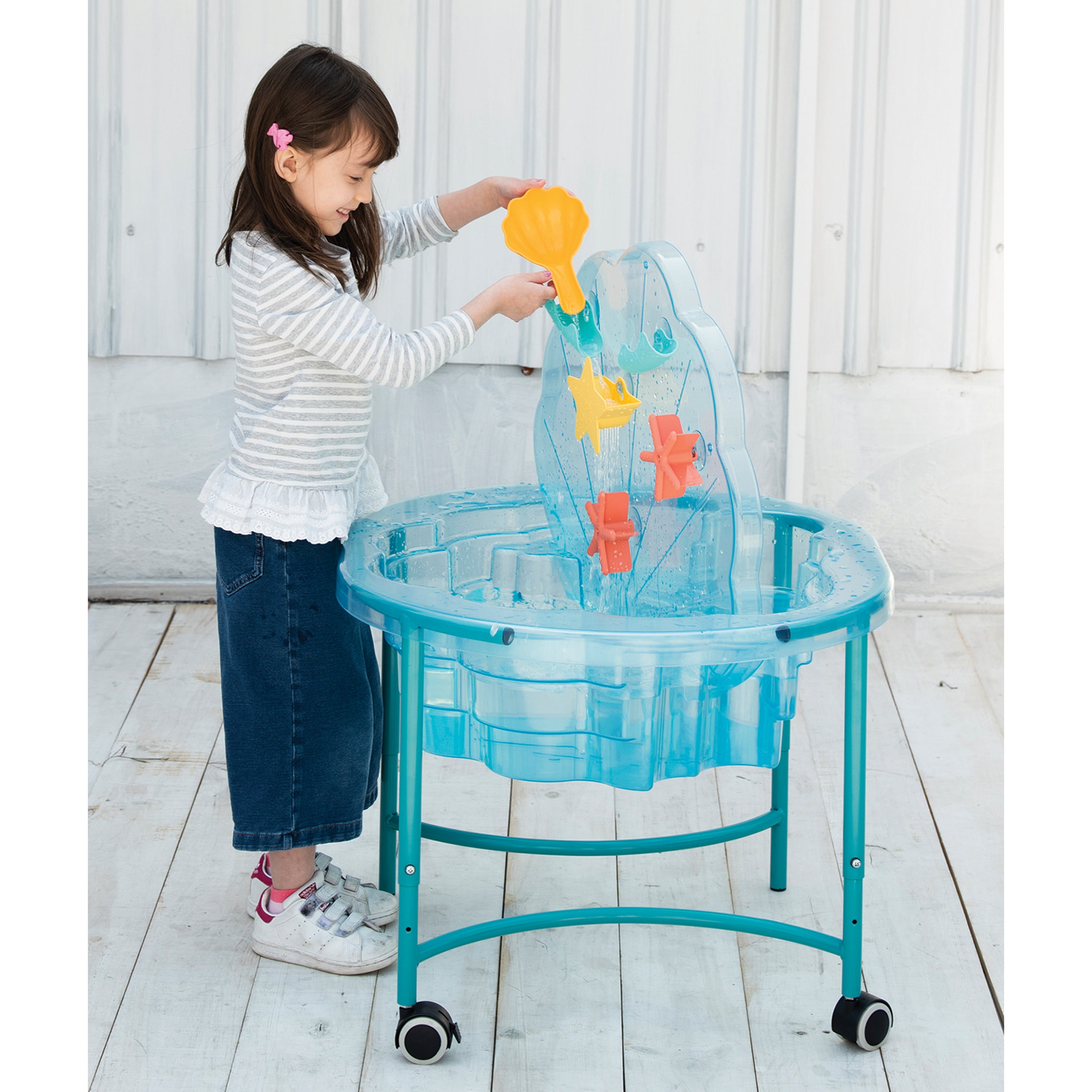 Child playing with a transparent blue water table on a wooden floor.
