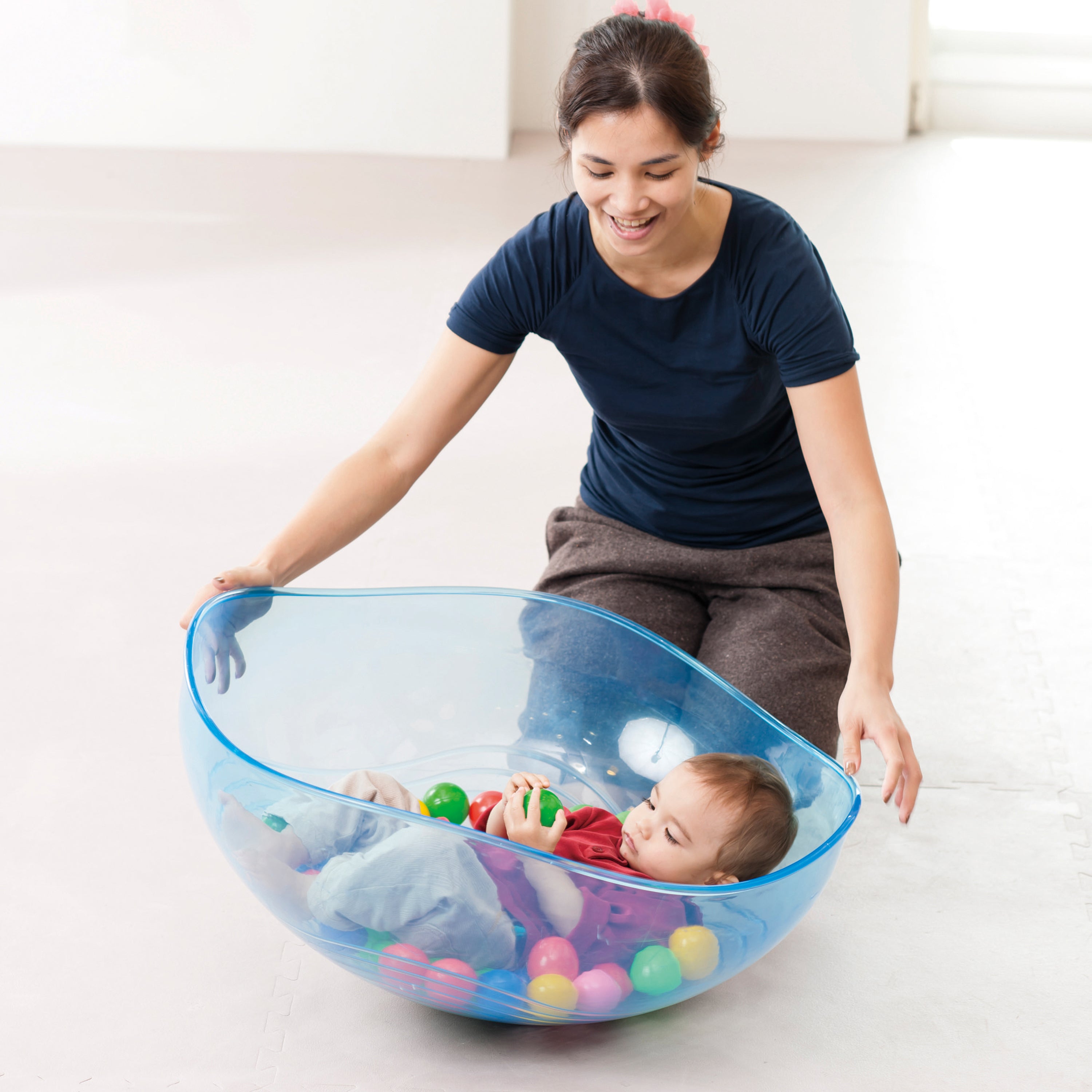 Woman playing with a child in a large blue plastic ball pit on a white floor.