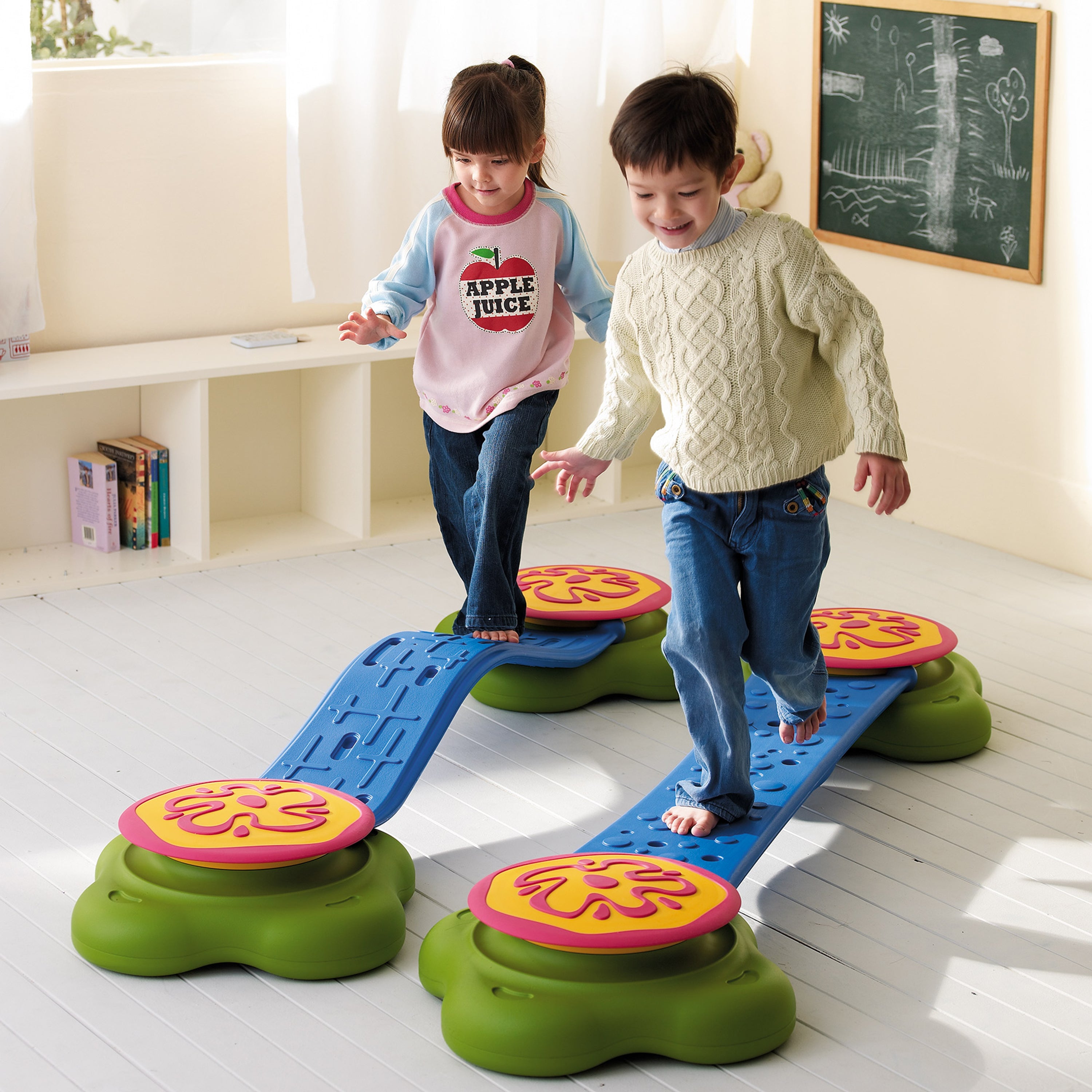Two children playing on a colorful balance beam toy indoors.