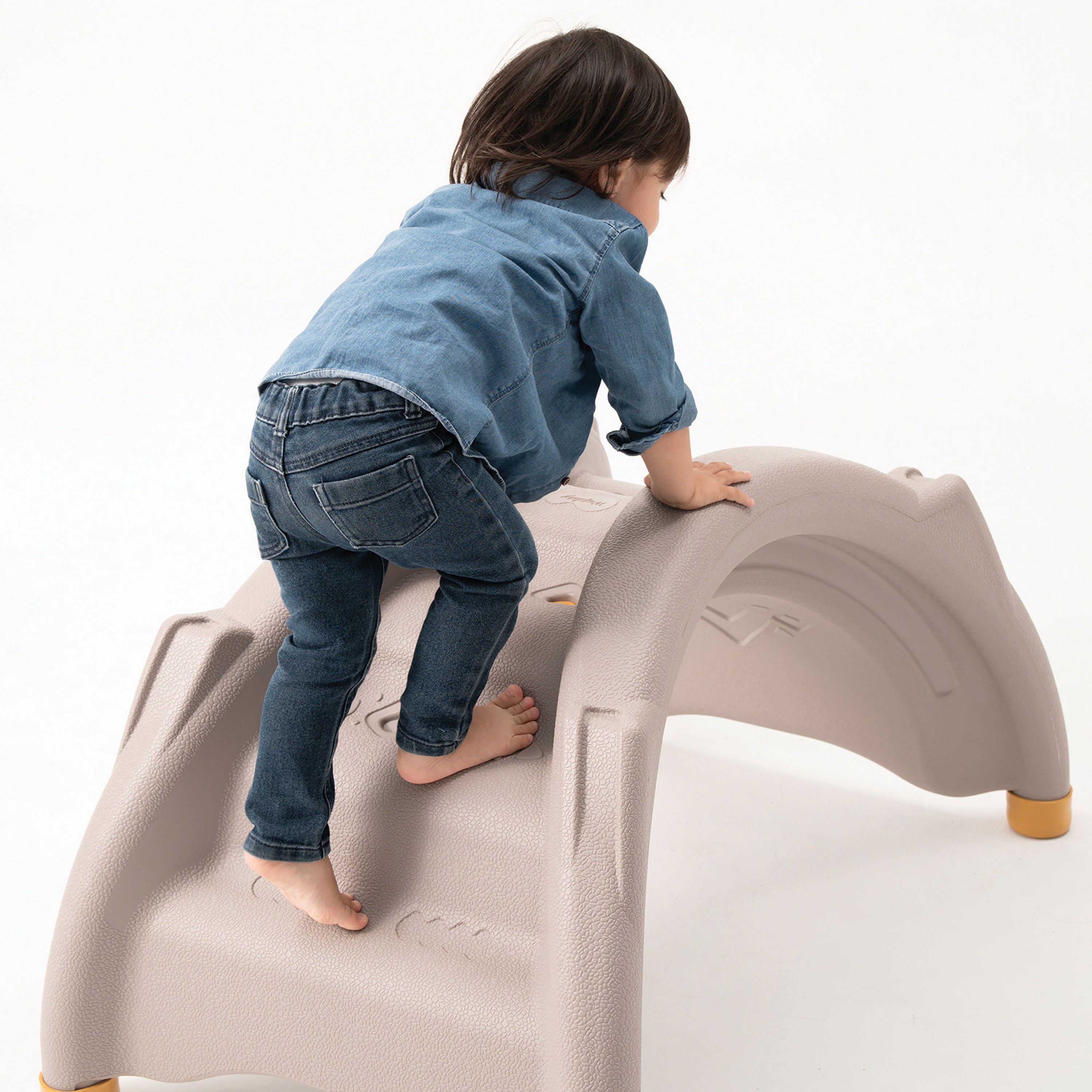 Child climbing on a beige plastic playground structure against a white background