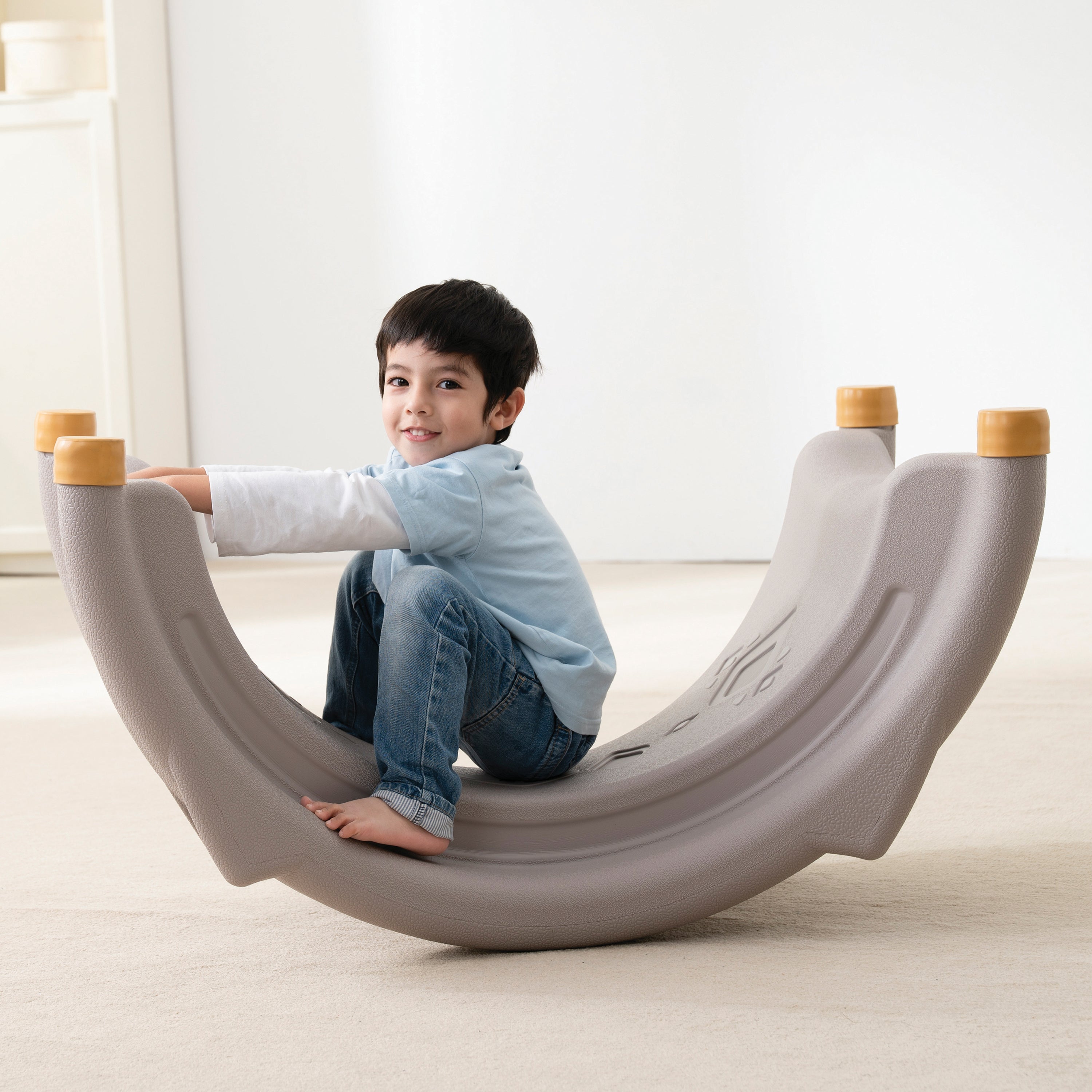 Child sitting on a gray rocker chair in a bright room.