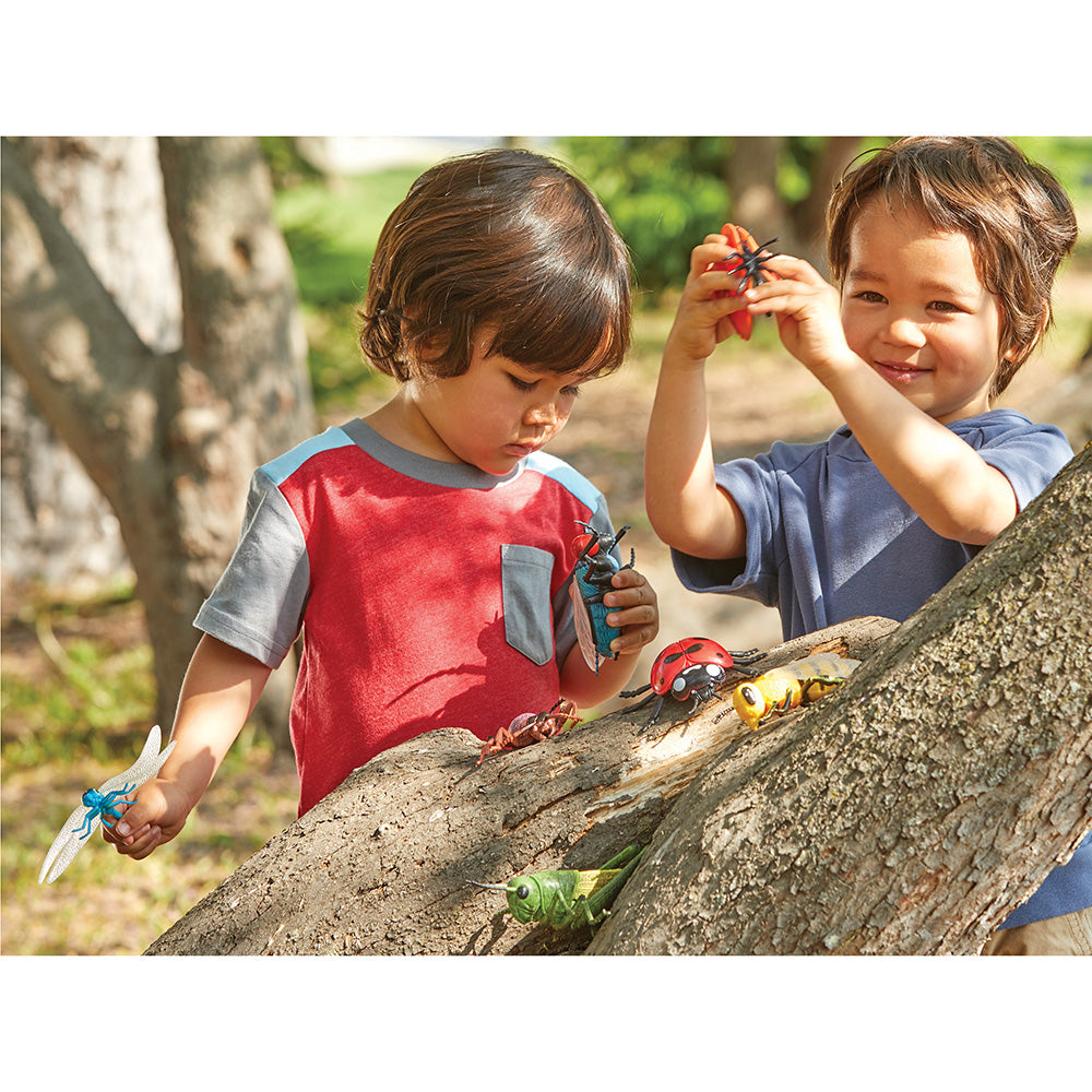 Two children playing with toy bugs on a tree branch outdoors.