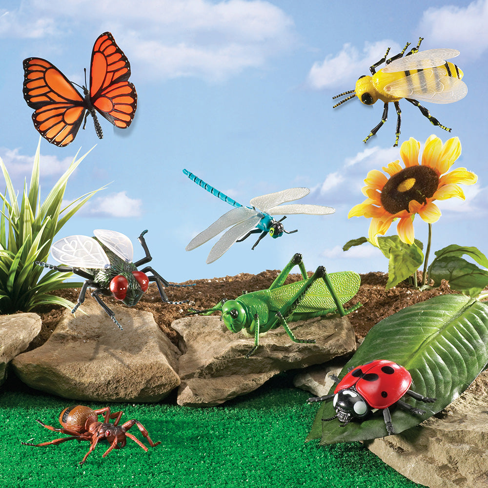 Assorted toy insects and a flower on a grassy area with a blue sky background