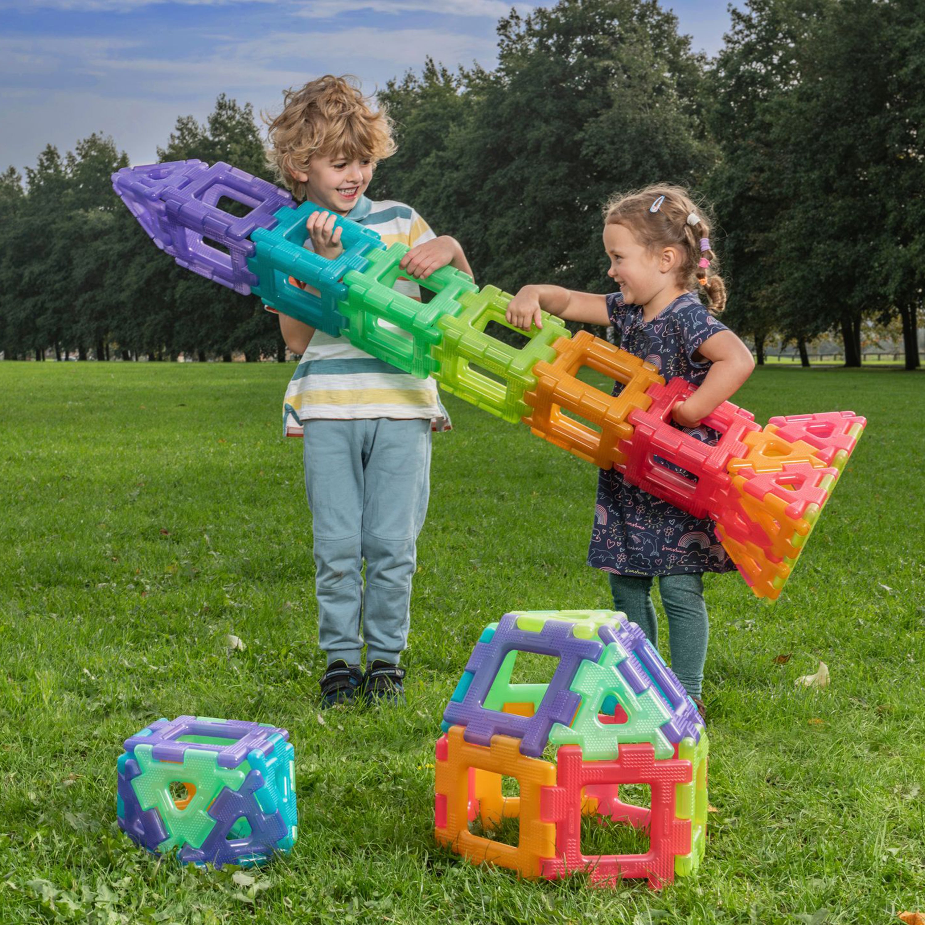 Two children playing with colorful building blocks on a grassy field.