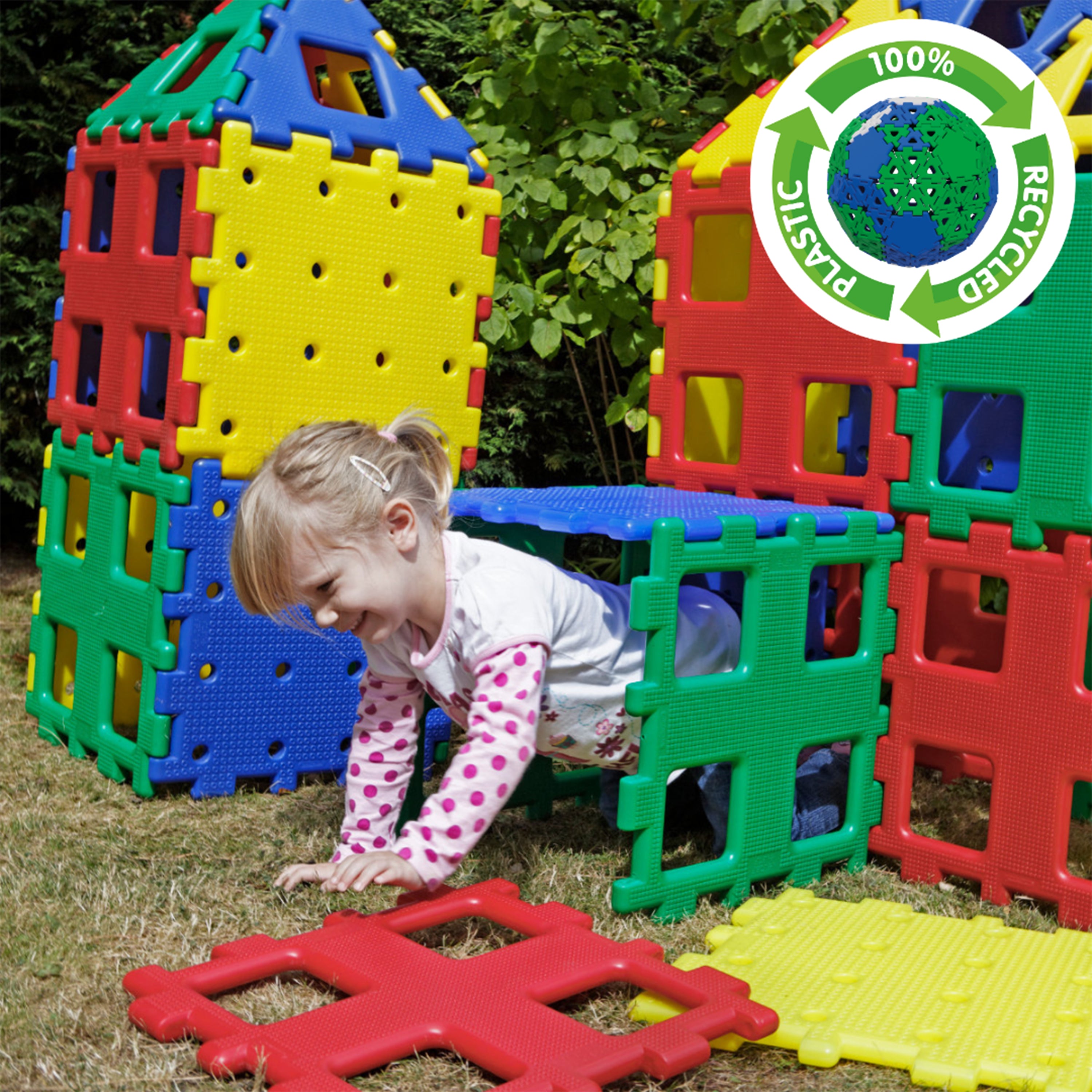 Child playing with colorful plastic building blocks on grass, with a recycling logo in the corner.