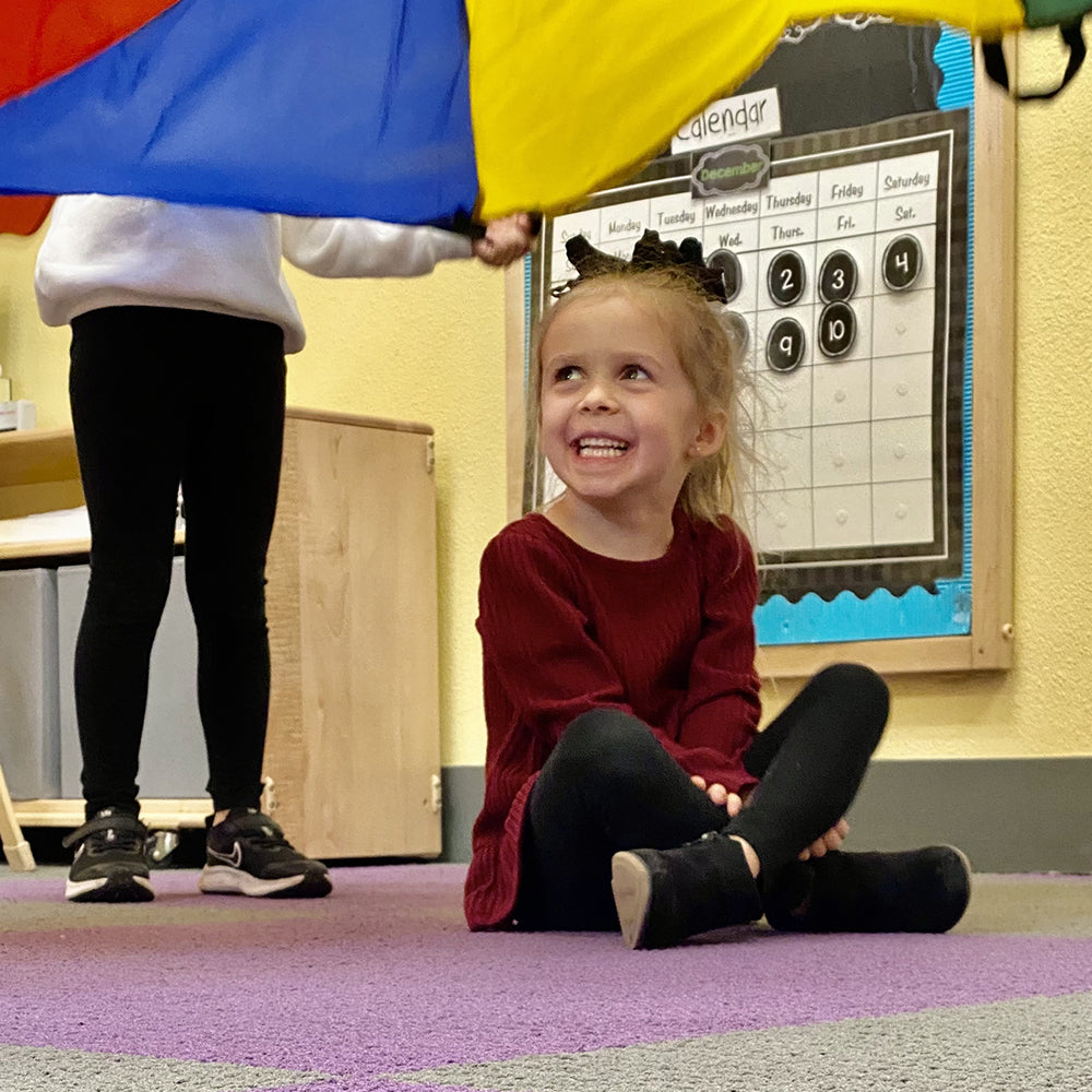 Kid Seated on Floor of Classroom Under Play Parachute