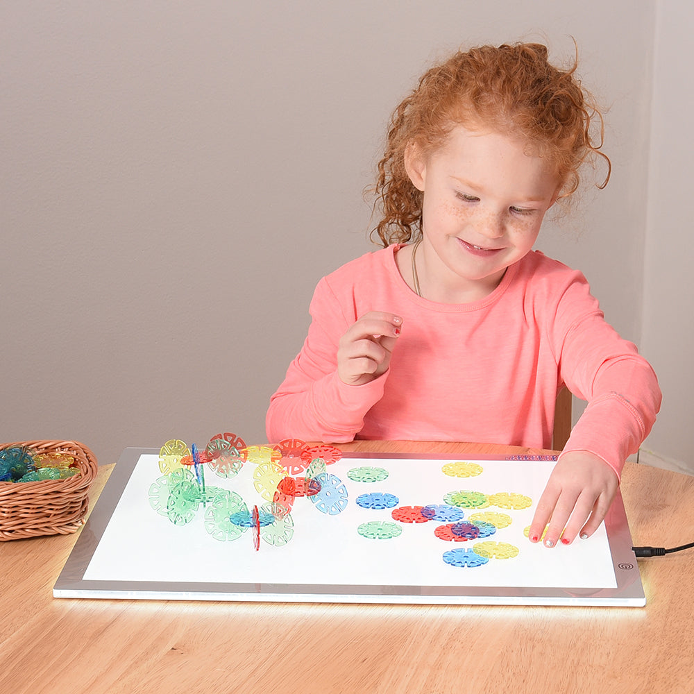Kid playing with colorful discs on light table in classroom