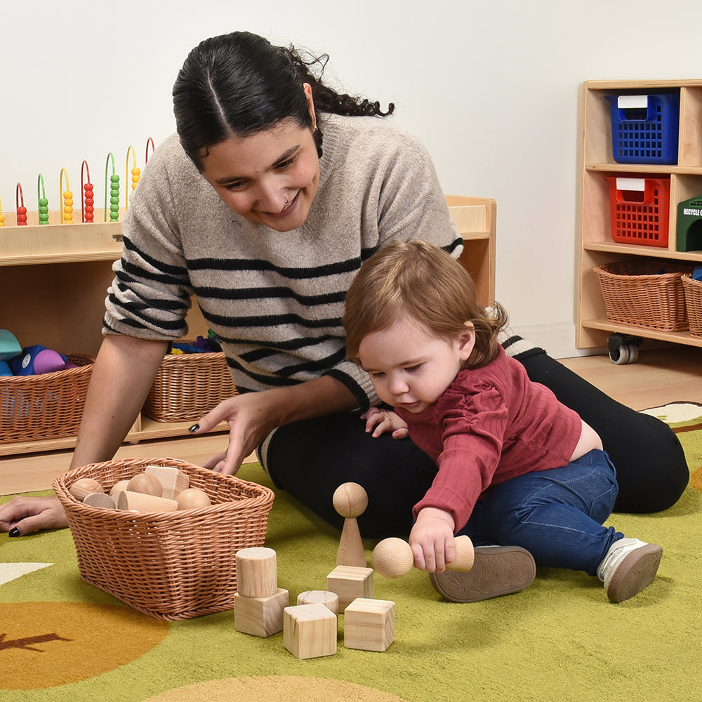 Infant & Teacher playing with wooden blocks in a classroom environment