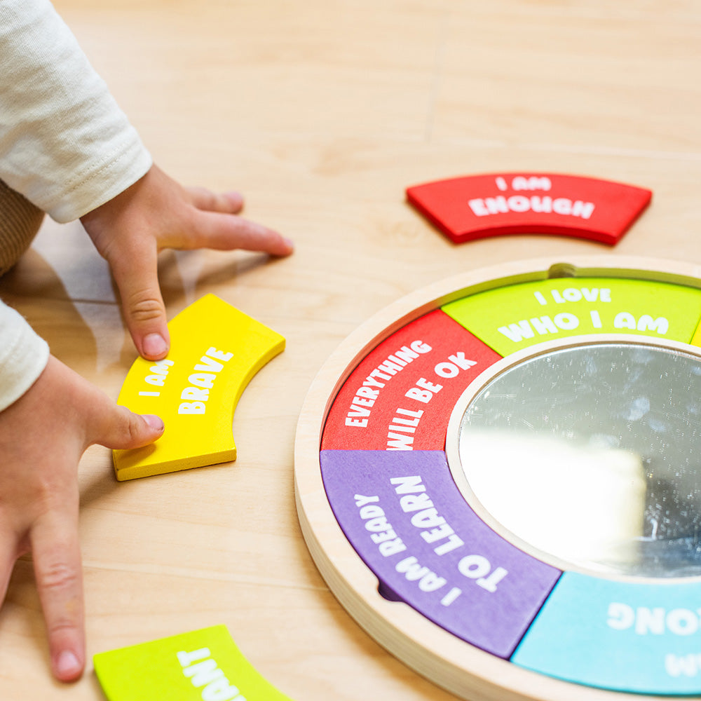 Children's hands interacting with a colorful wooden wheel on a light wood surface.