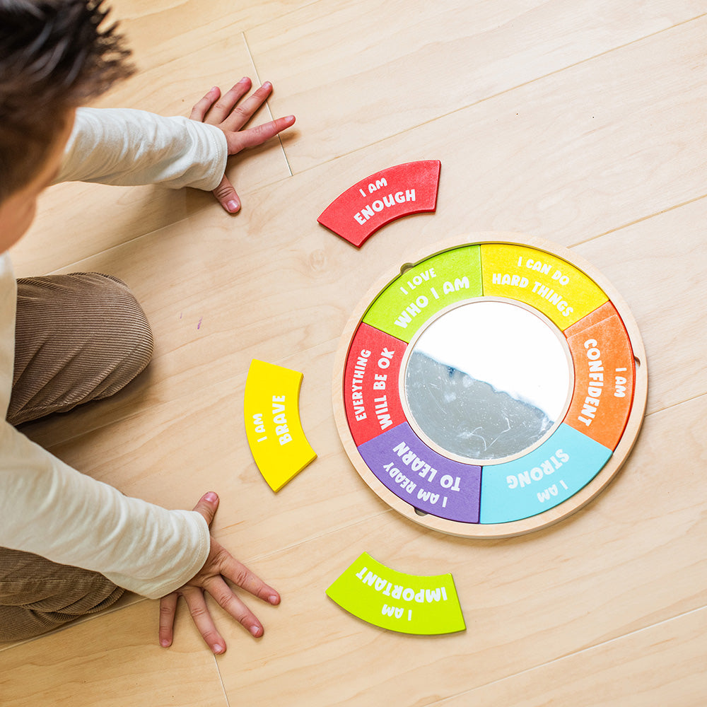 Child playing with a colorful circular mirror on a wooden floor