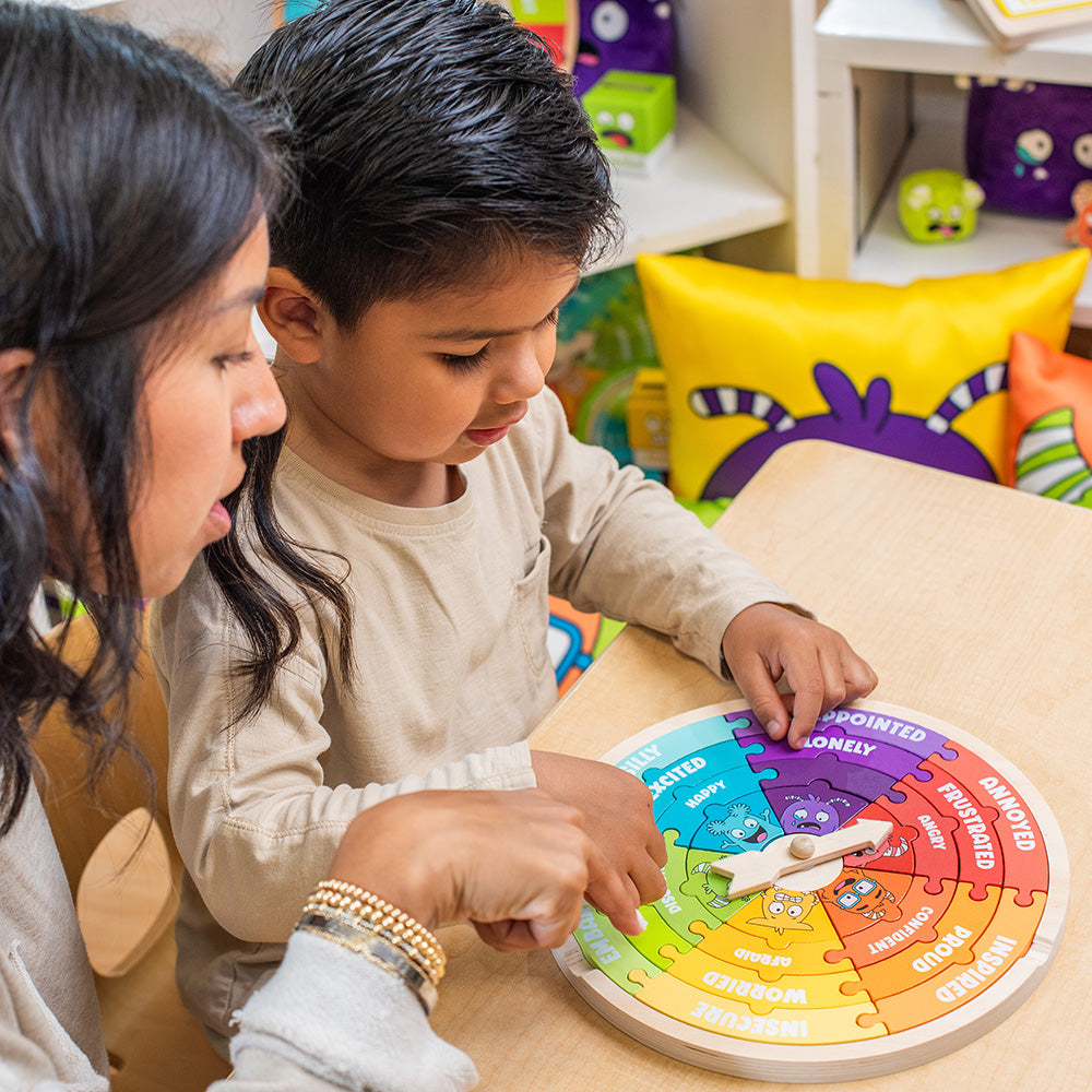 Woman and child playing with a colorful emotion wheel puzzle at a table.