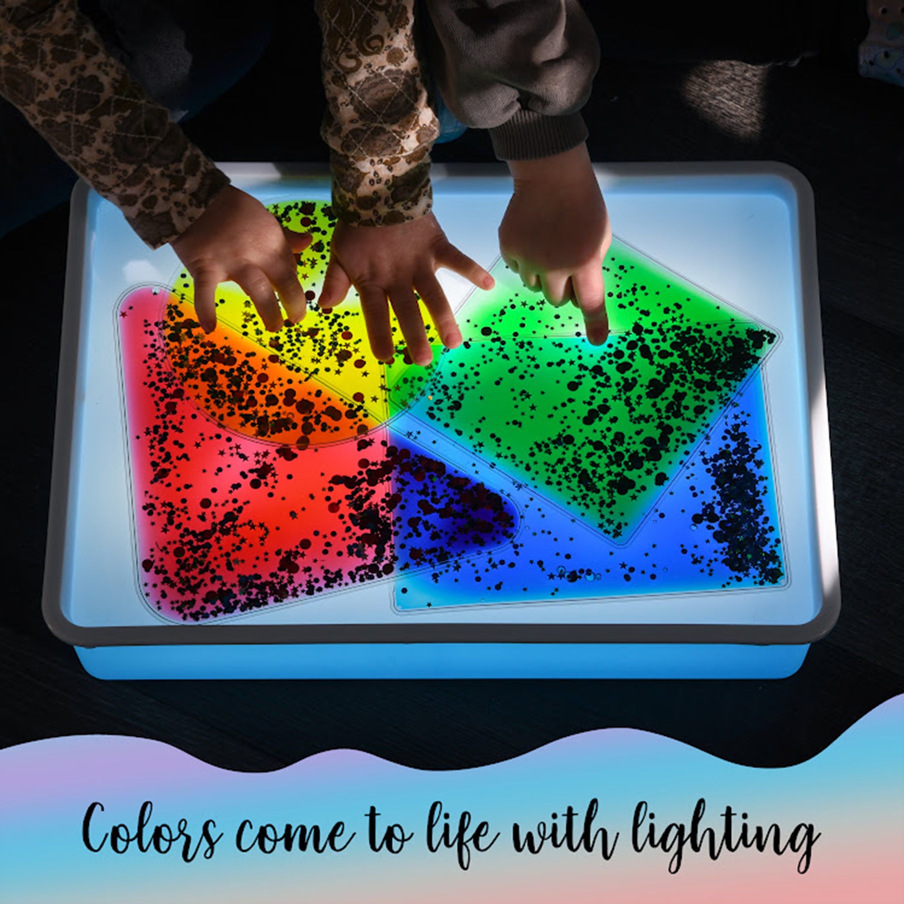 Children's hands interacting with a colorful light-up tray filled with translucent shapes