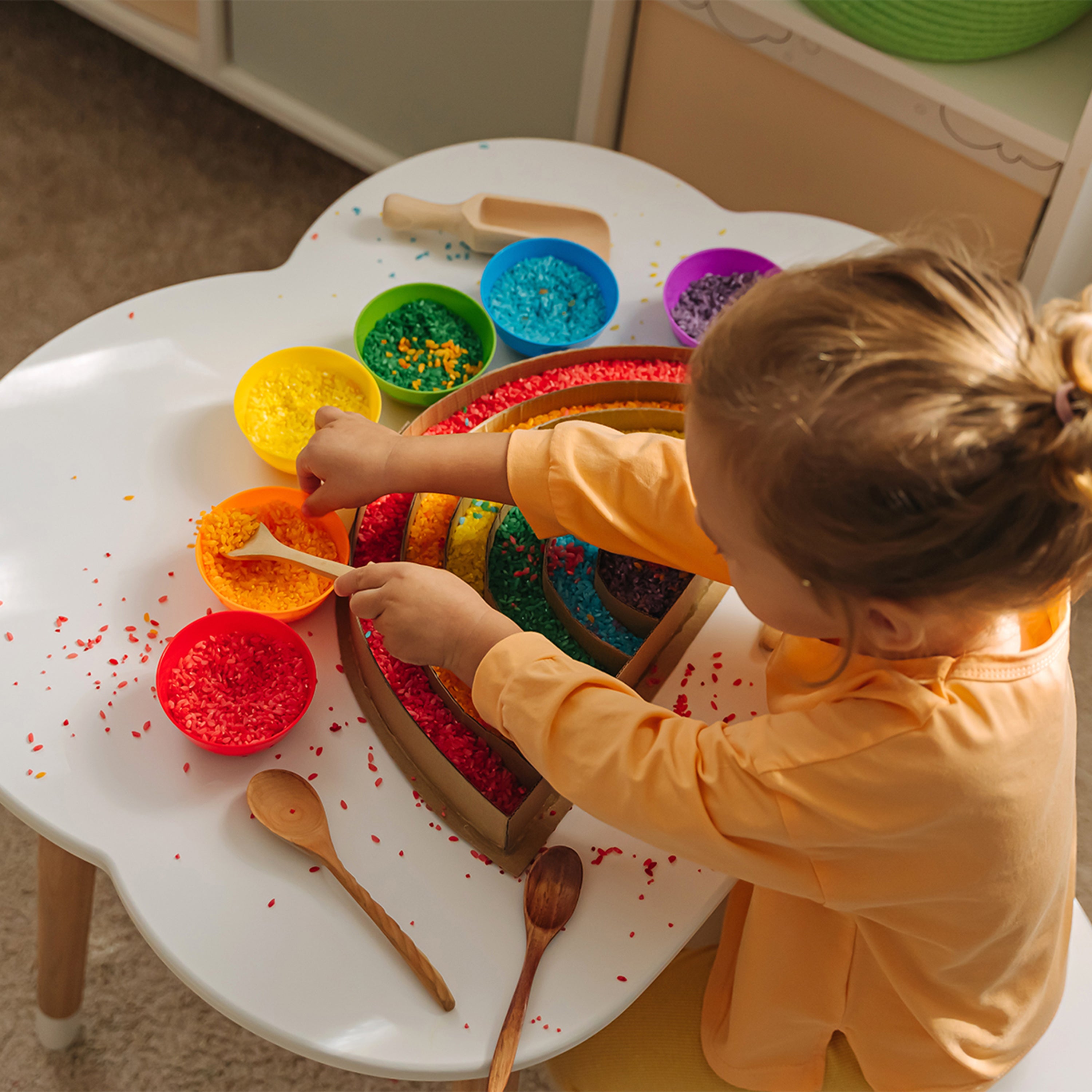 Child playing with colorful play rice and tools on a white table.