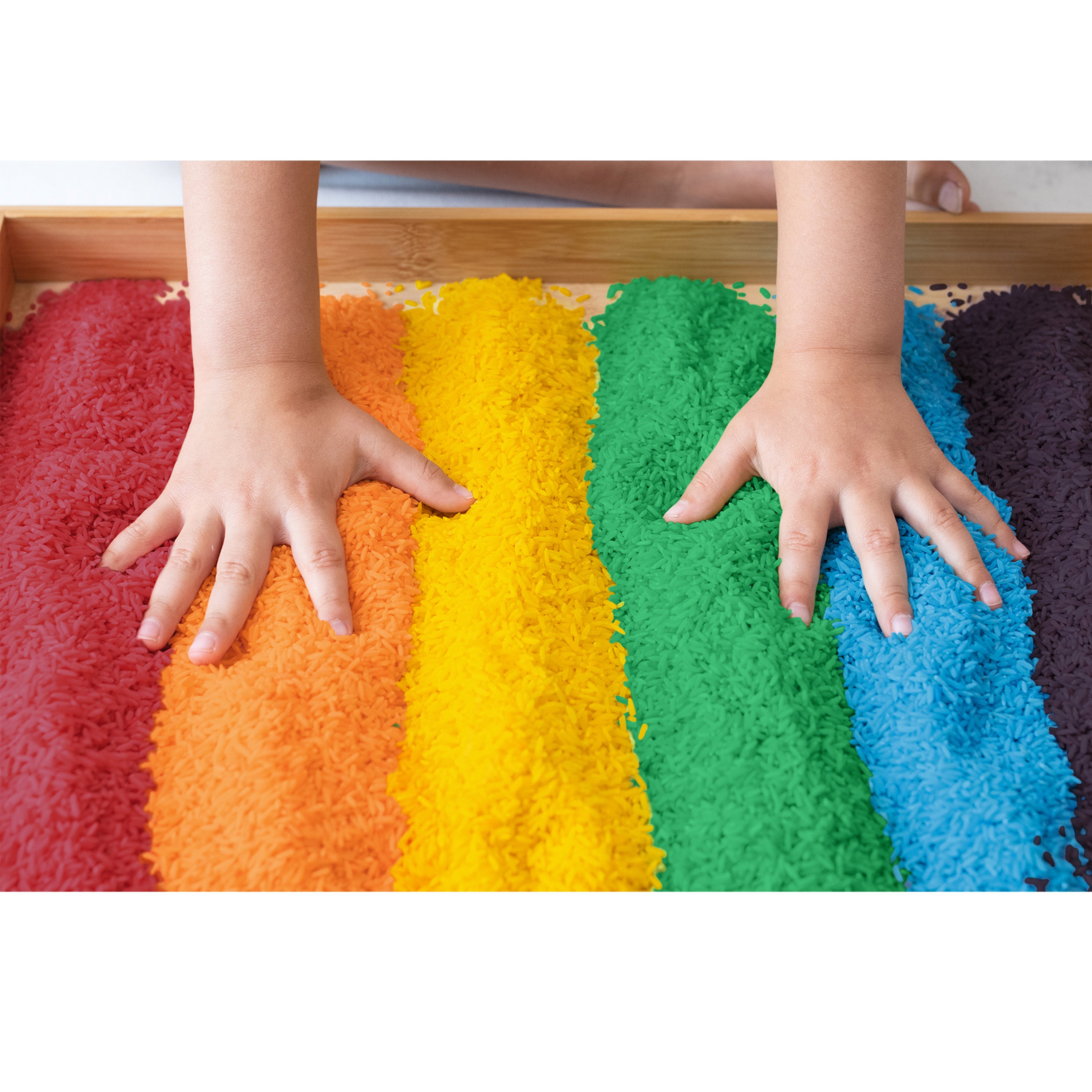 Children's hands on a rainbow-colored sand tray