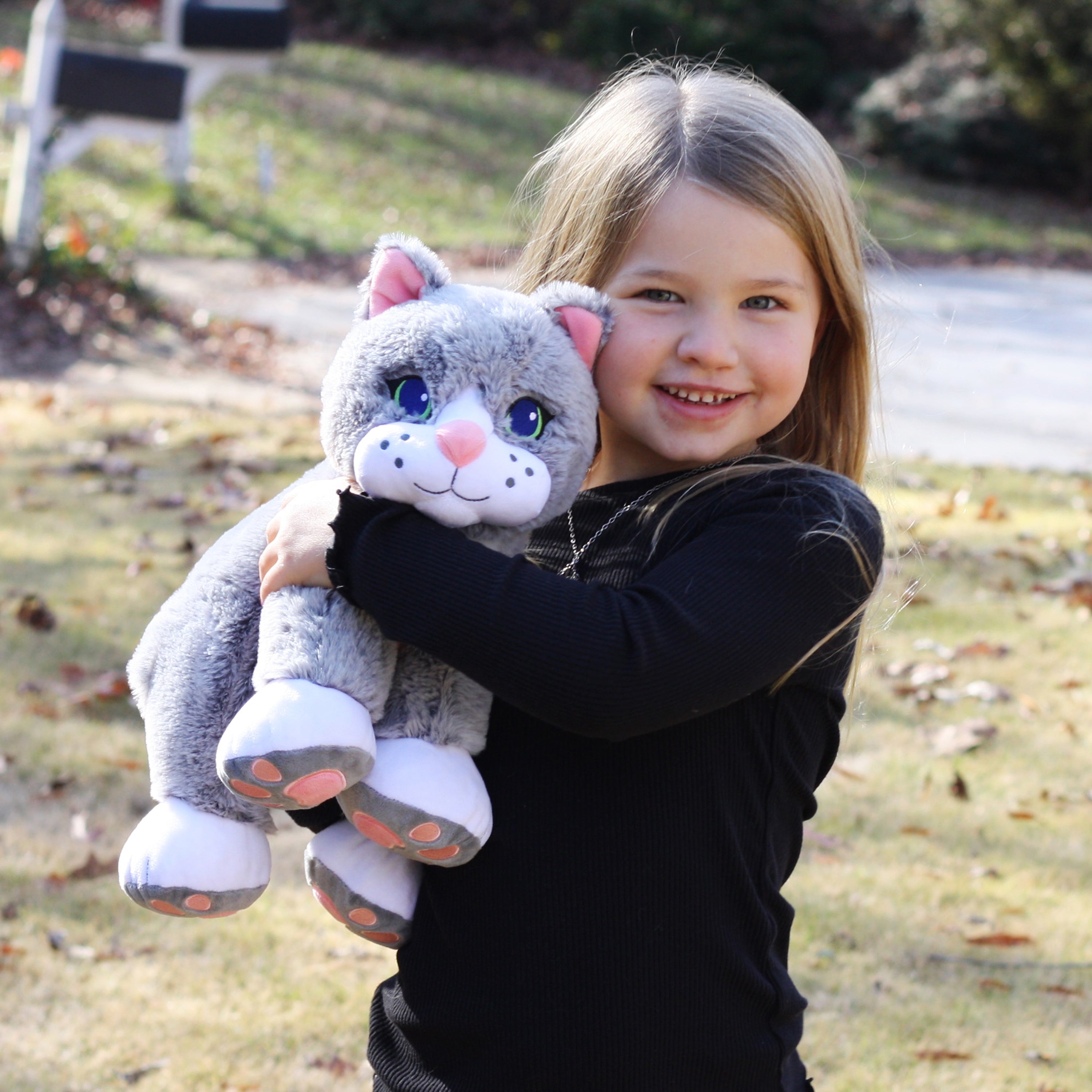 Child holding a plush toy cat outdoors on a sunny day