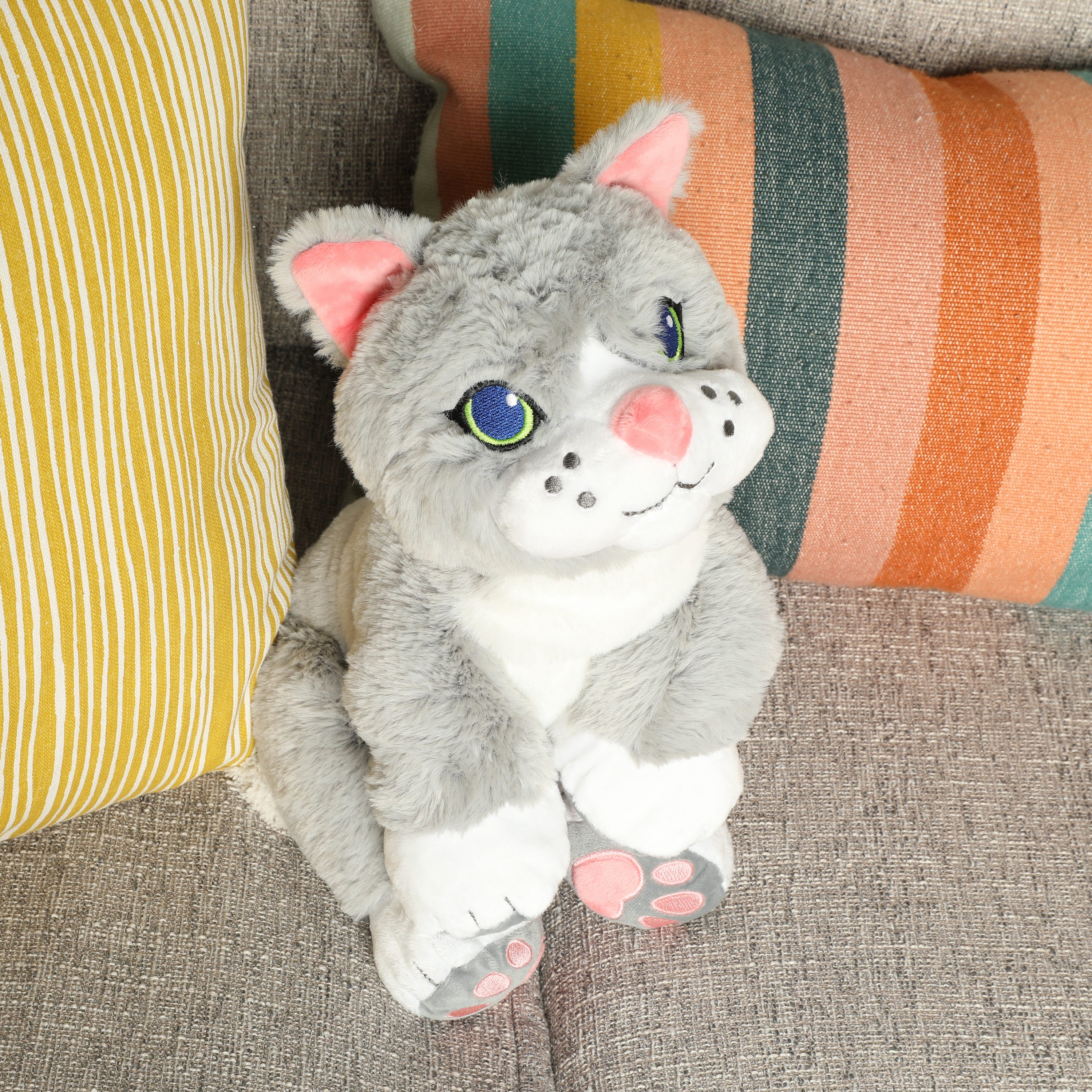 Plush toy cat on a textured surface with colorful pillows in the background