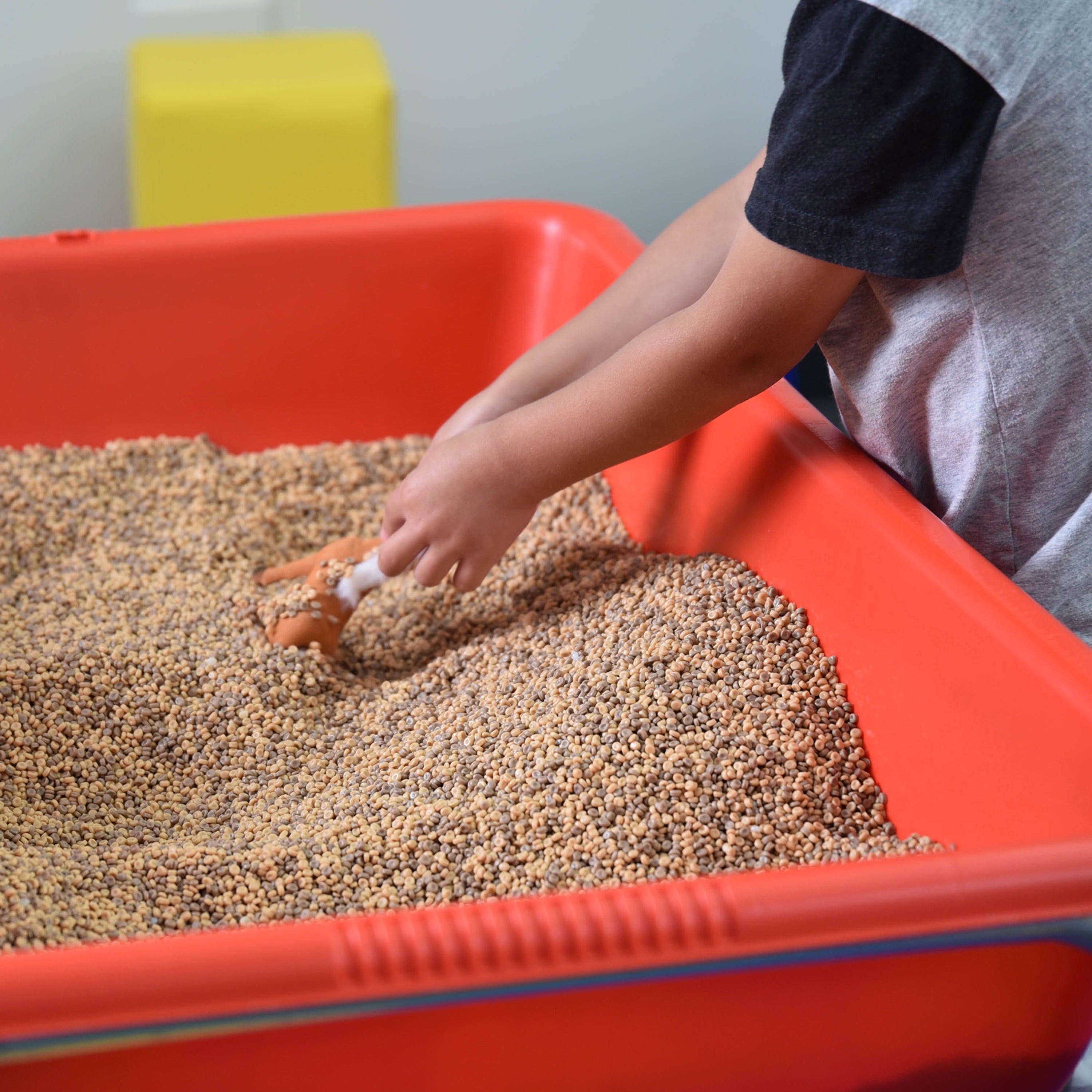 Child playing with sand in a red tray