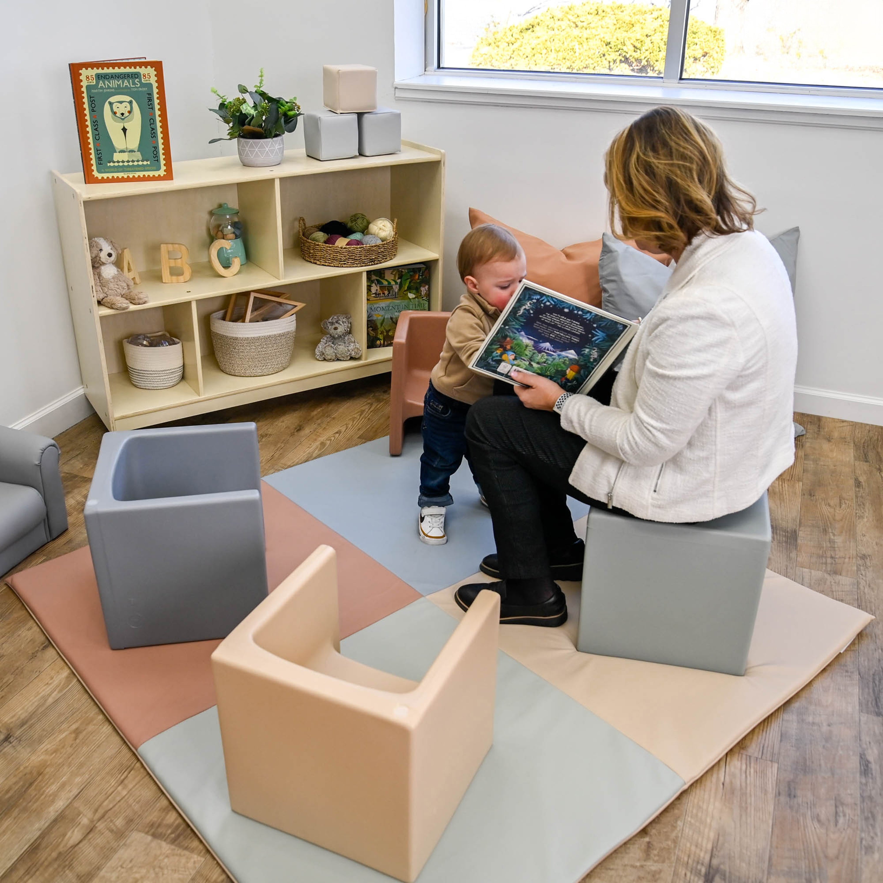 Woman reading a book to a child in a cozy room with colorful flooring and shelves.