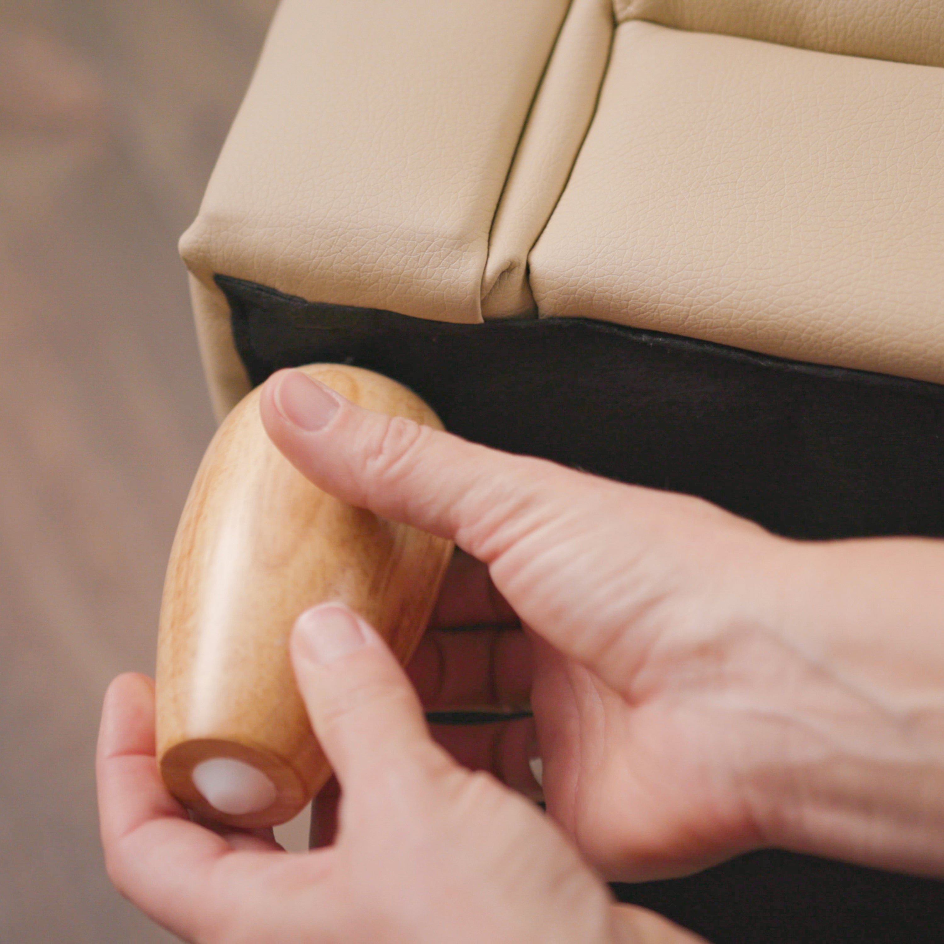 Hand holding a wooden leg against a beige armchair