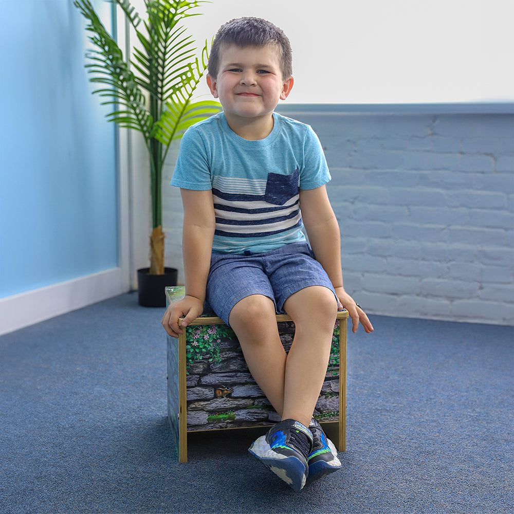 Child sitting on a small wooden stool with a blue wall and plant in the background