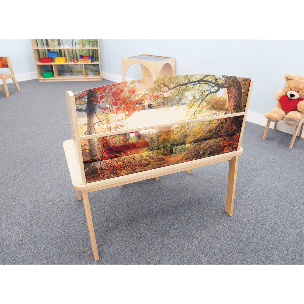 Children's play area with a wooden table featuring a nature-themed cover in a classroom setting.