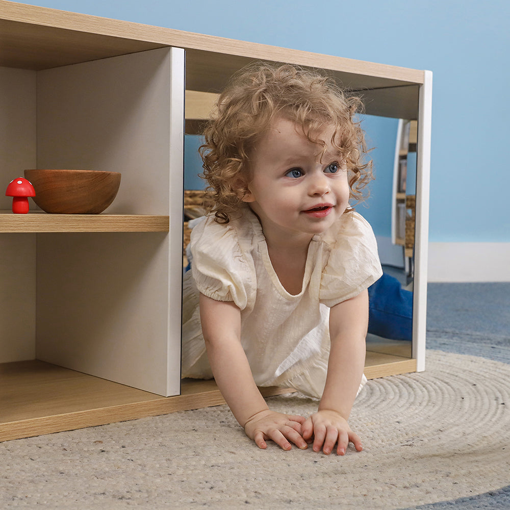 Child peeking out from behind a wooden shelf with a blue wall in the background